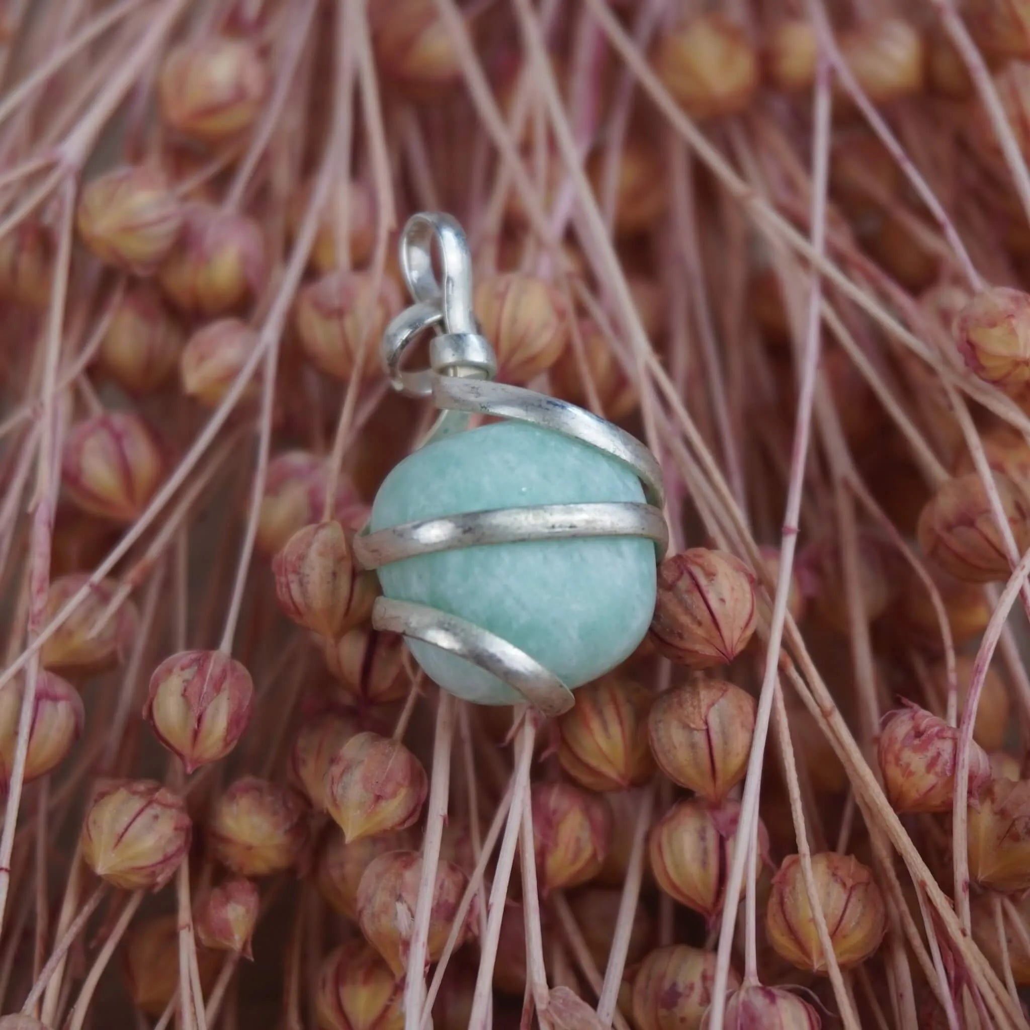 Amazonit Kettenanhänger mit Silberfassung vor rosa Trockenblumen arrangiert