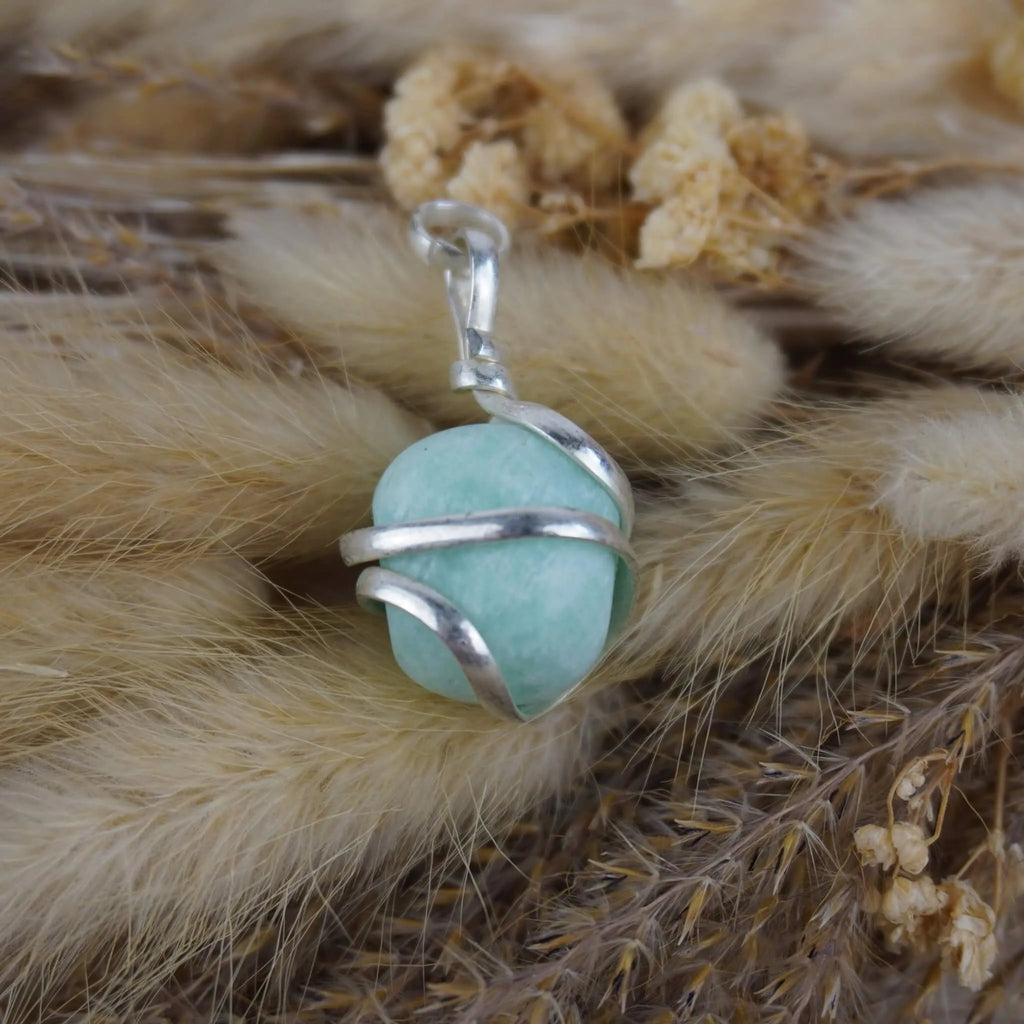 Amazonit Kettenanhänger mit silberner Spiralfassung auf beigen Trockenpflanzen