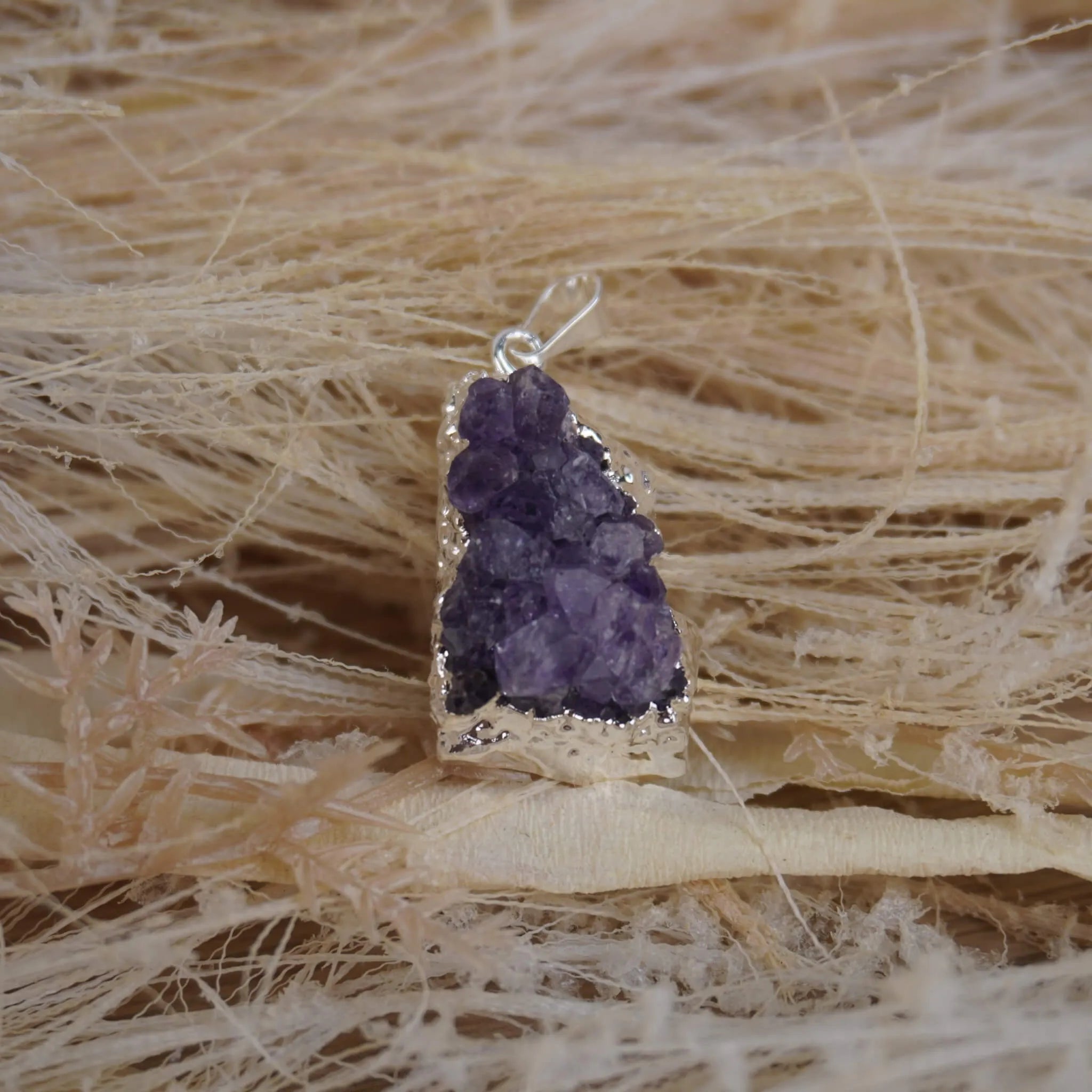Amethyst Druse Kettenanhänger mit silberner Umrandung auf hellen Naturfasern arrangiert