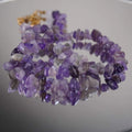 Amethyst Halskette mit violetten Splittersteinen auf spiegelnder Fläche, goldener Verschluss im Hintergrund
