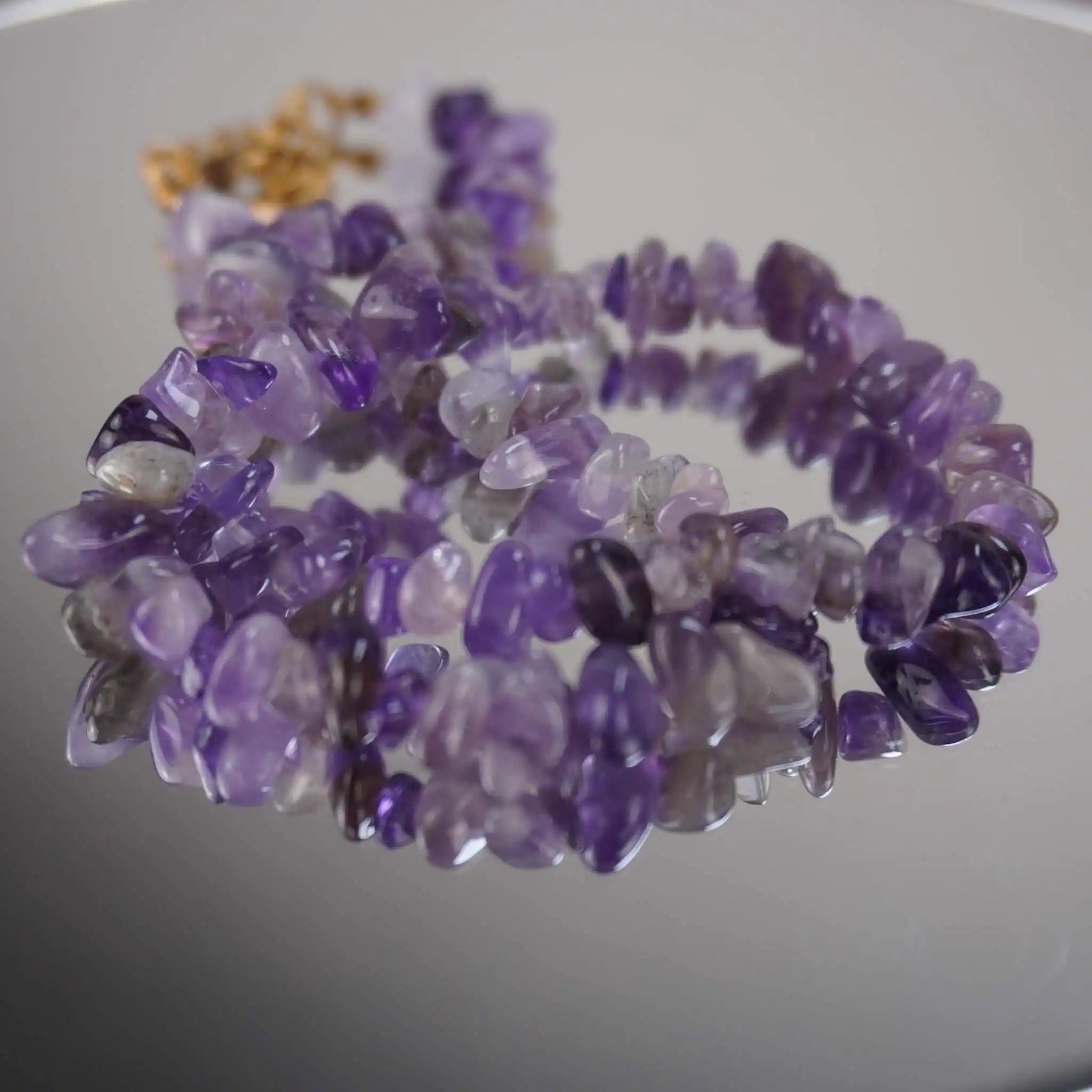 Amethyst Halskette mit violetten Splittersteinen auf spiegelnder Fläche, goldener Verschluss im Hintergrund