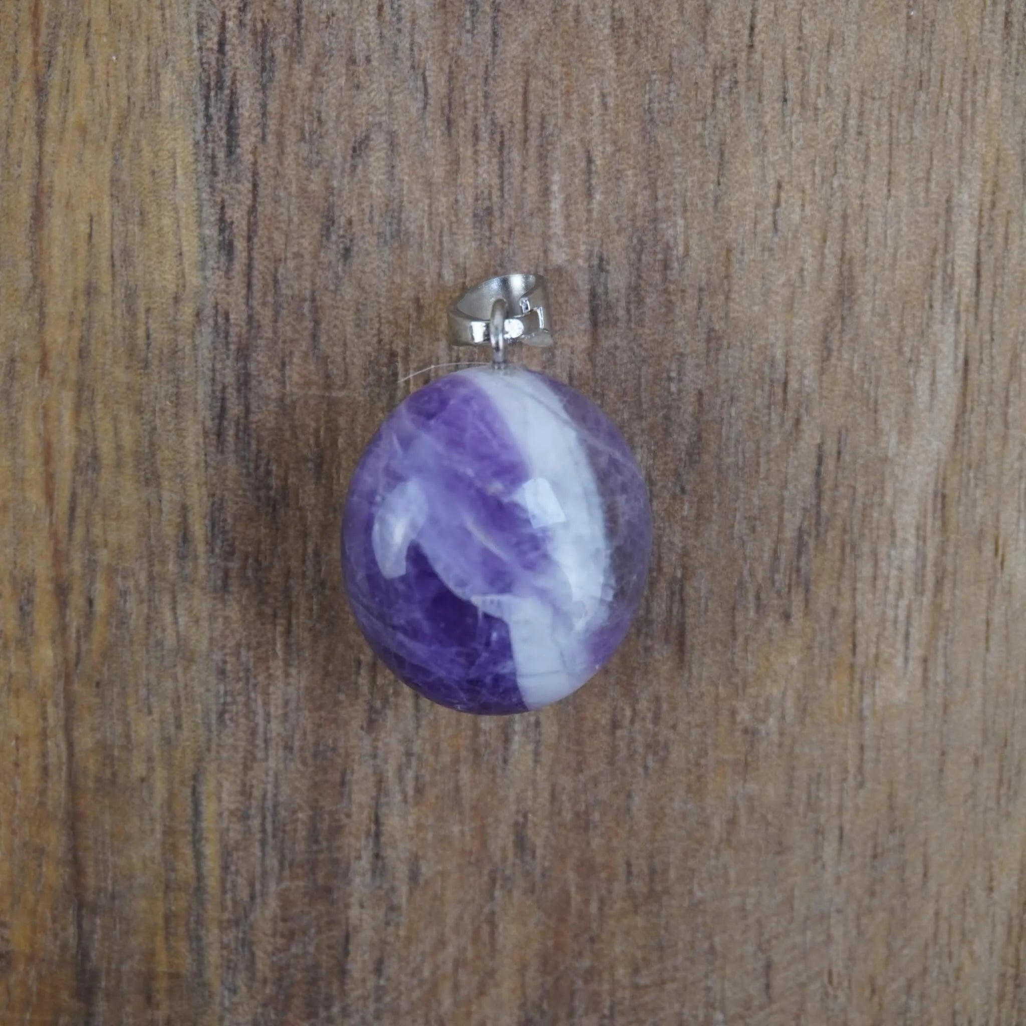 Amethyst Kettenanhänger mit silberner Öse liegend auf rustikalem Holzuntergrund