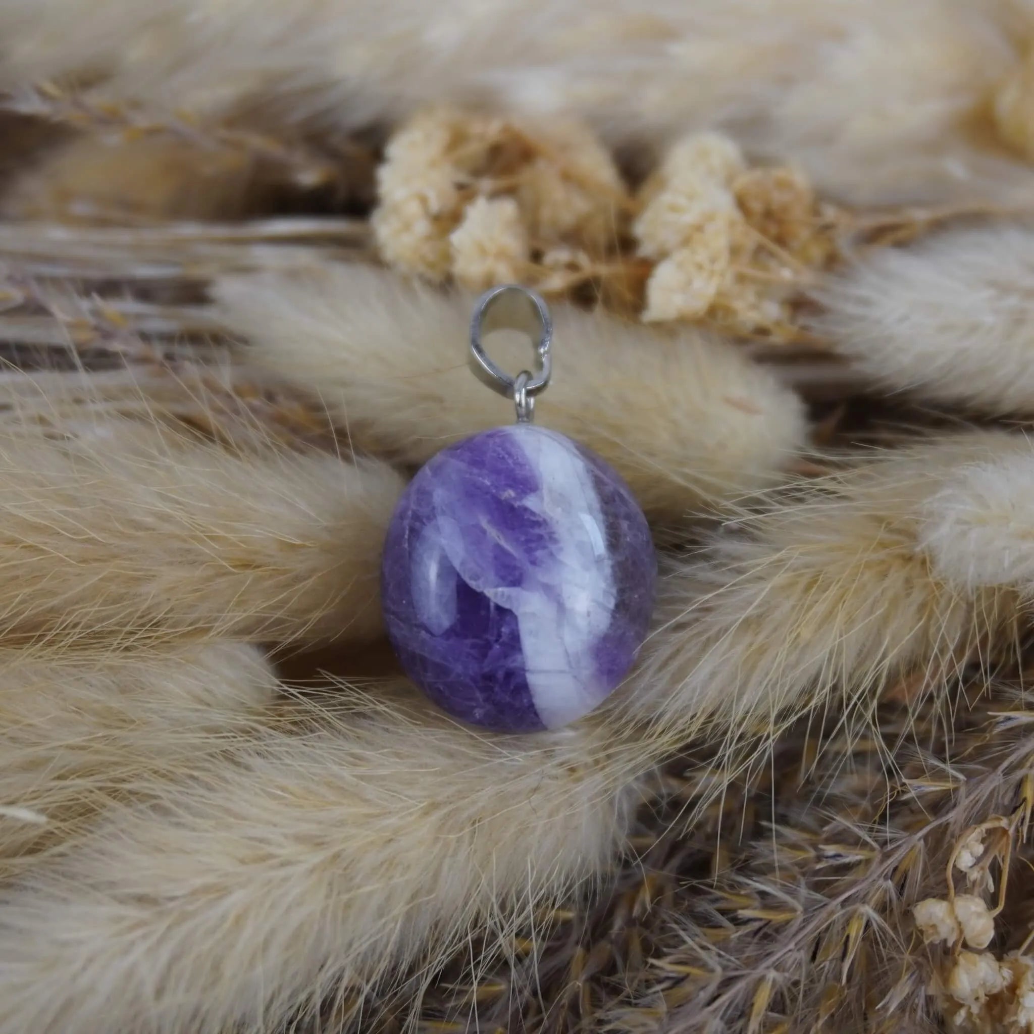 Amethyst Kettenanhänger mit silberfarbener Öse auf beigen Trockenpflanzen