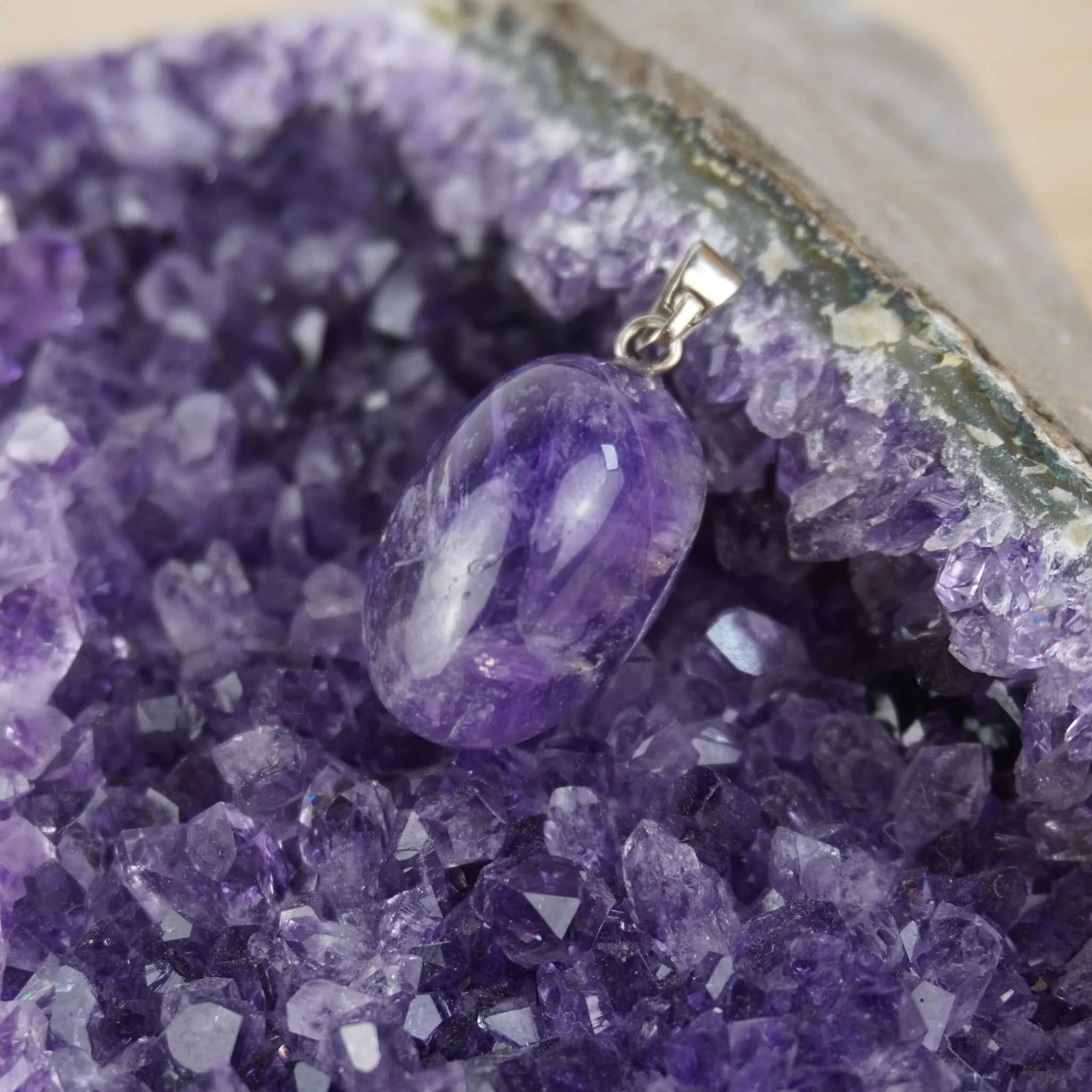 Amethyst Trommelstein Kettenanhänger mit silberner Öse präsentiert auf Amethyst-Druse