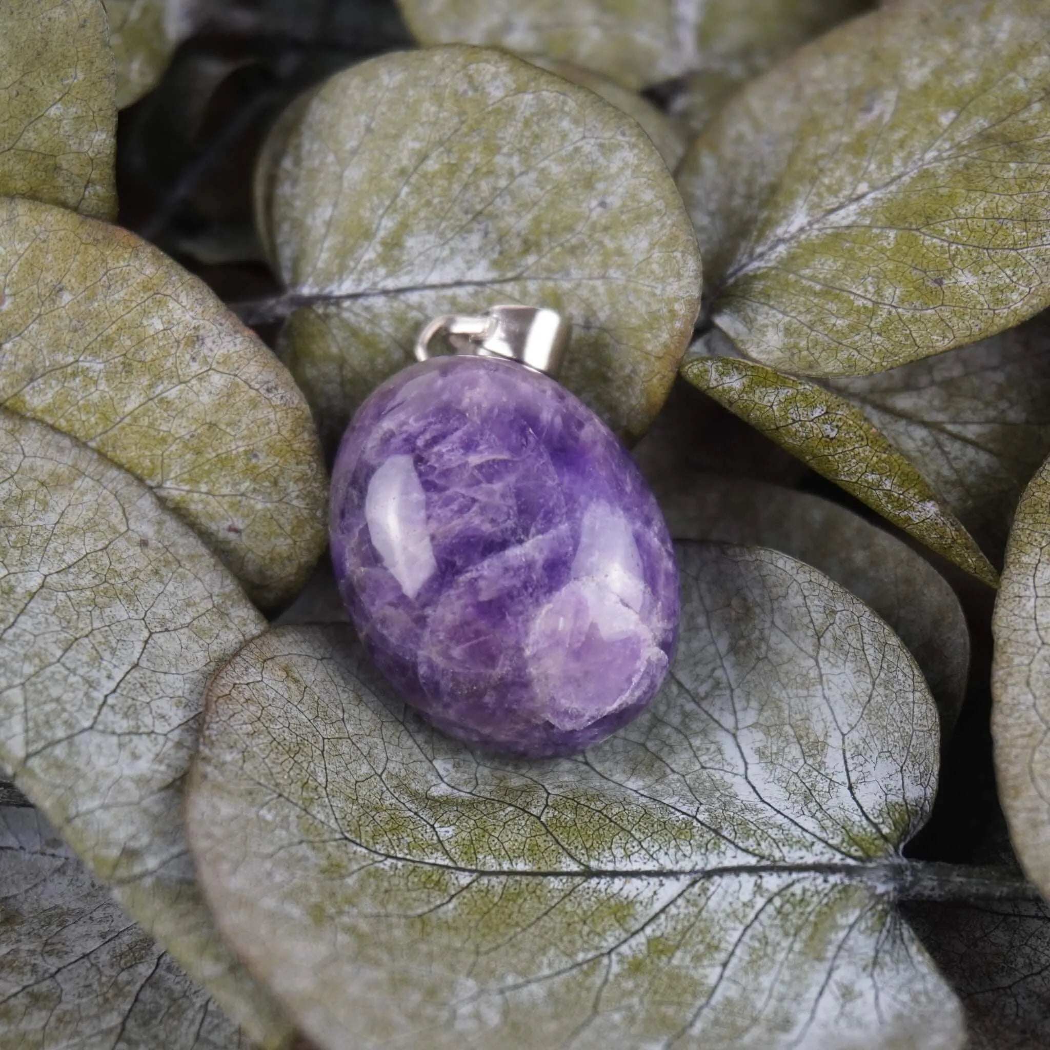 Amethyst Trommelstein Kettenanhänger mit Silber Öse auf grünen Eukalyptusblättern dekoriert