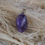 Amethyst Trommelstein Kettenanhänger mit silberner Öse dekoriert auf hellen Naturfasern