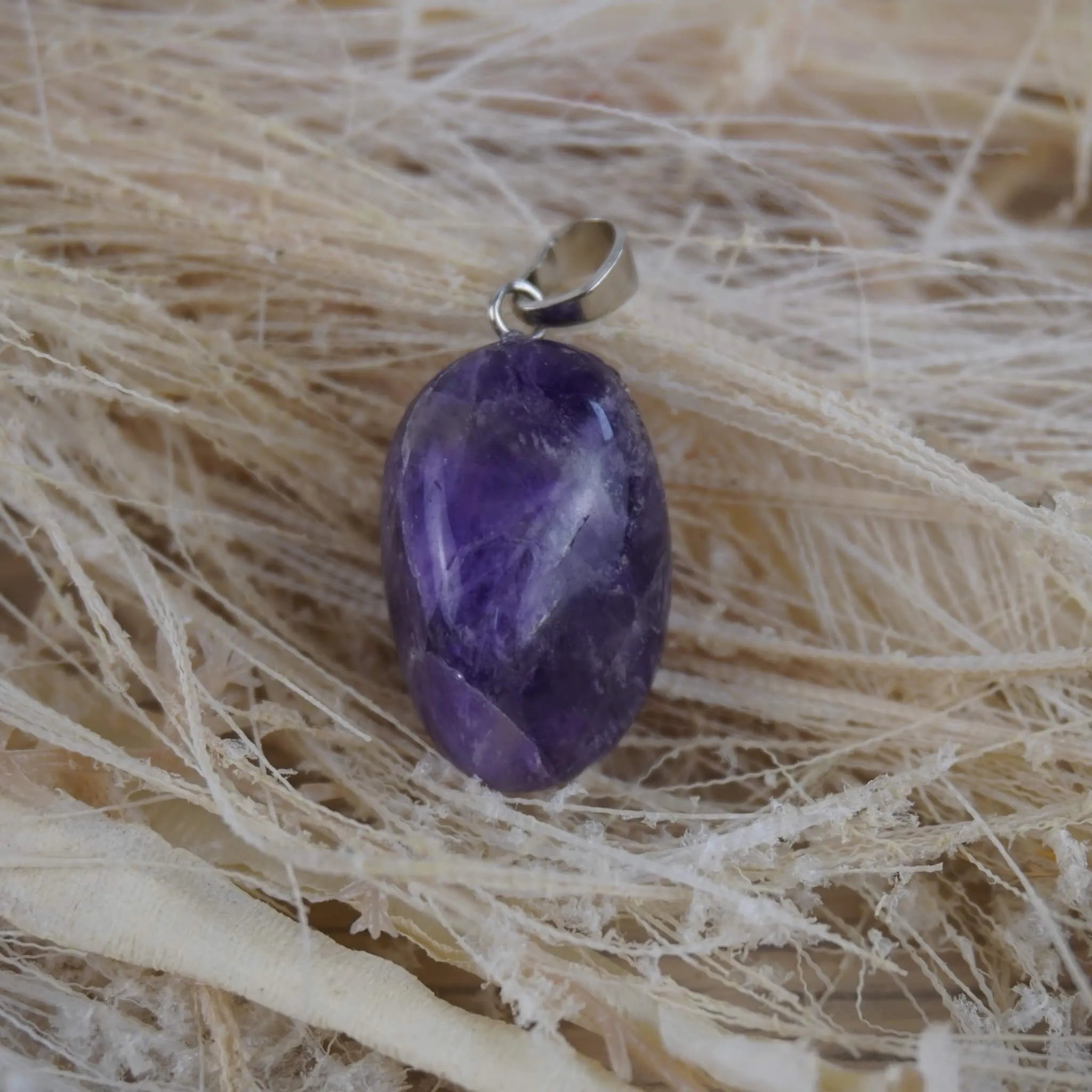 Amethyst Trommelstein Kettenanhänger mit silberner Öse dekoriert auf hellen Naturfasern