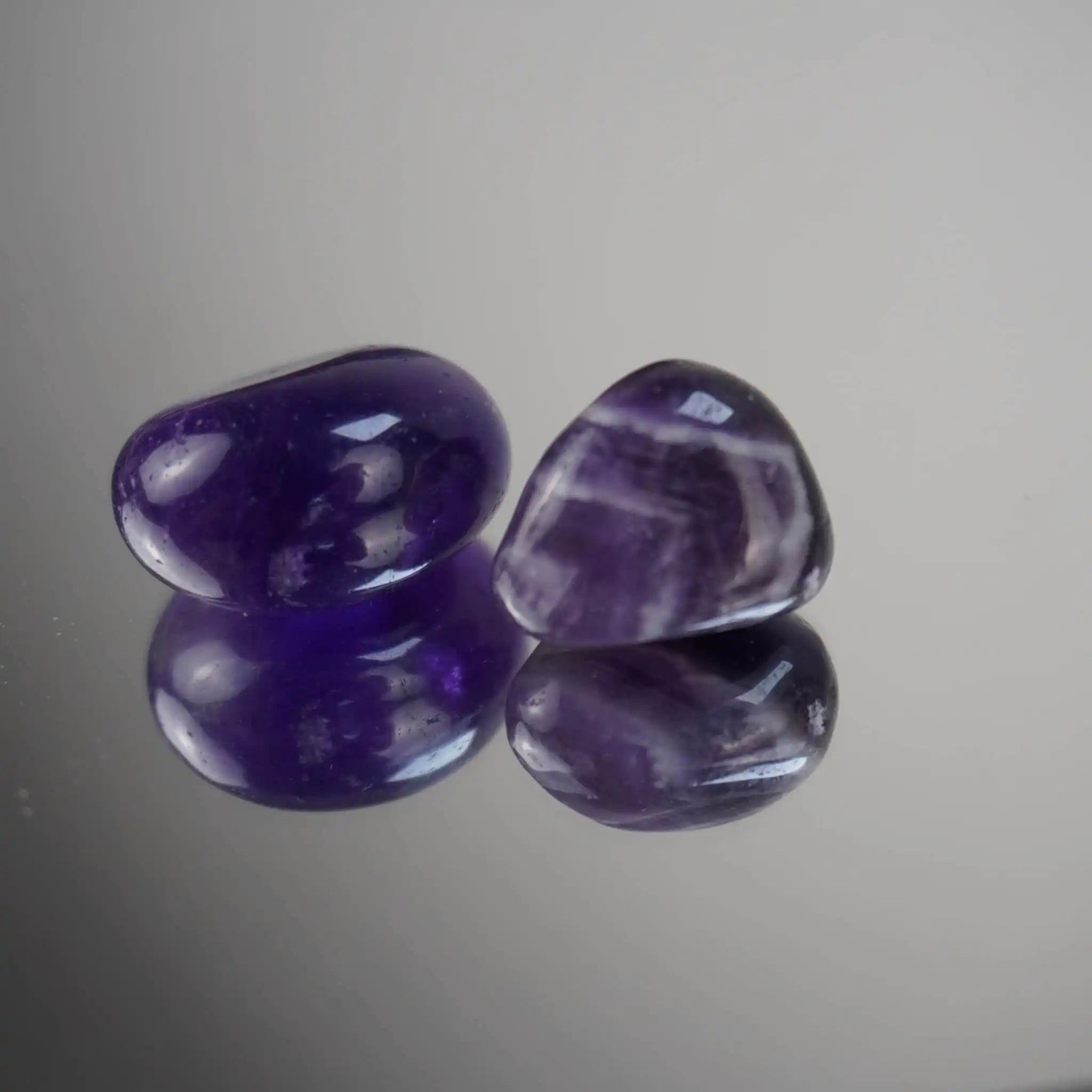 Zwei polierte Amethyst Trommelsteine klein auf einer spiegelnden Oberfläche