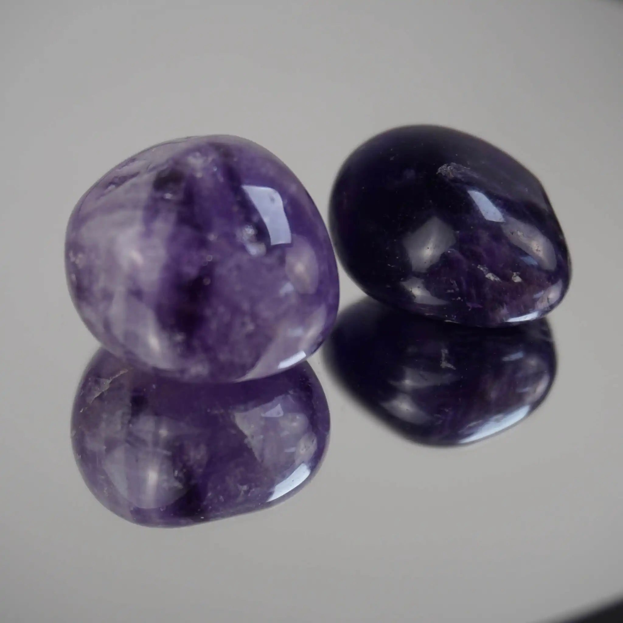 Zwei polierte Amethyst Trommelsteine mittel auf einer spiegelnden Oberfläche