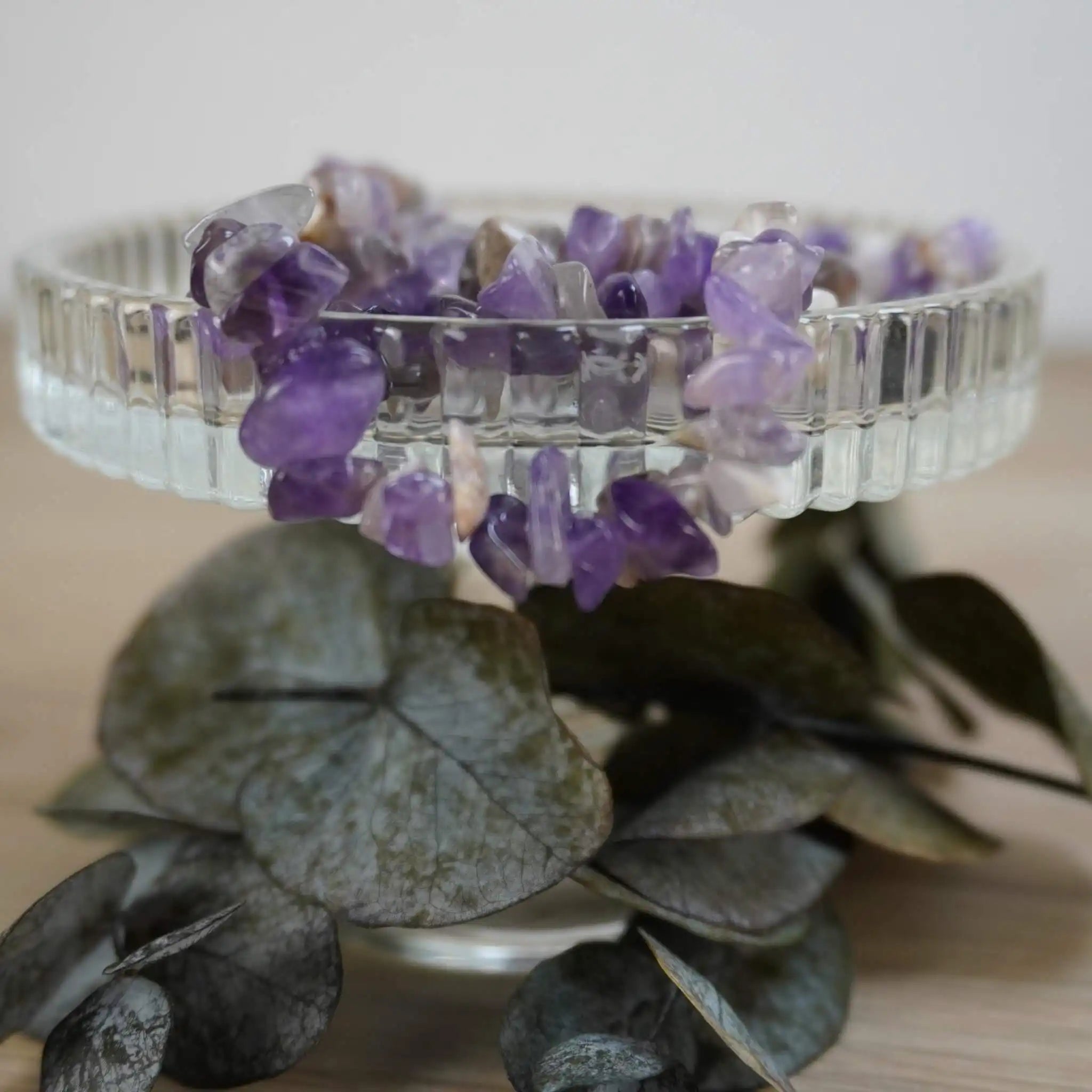 Amethyst Splitterarmband auf gläserner Schmuckschale, dekoriert mit grünen Blättern