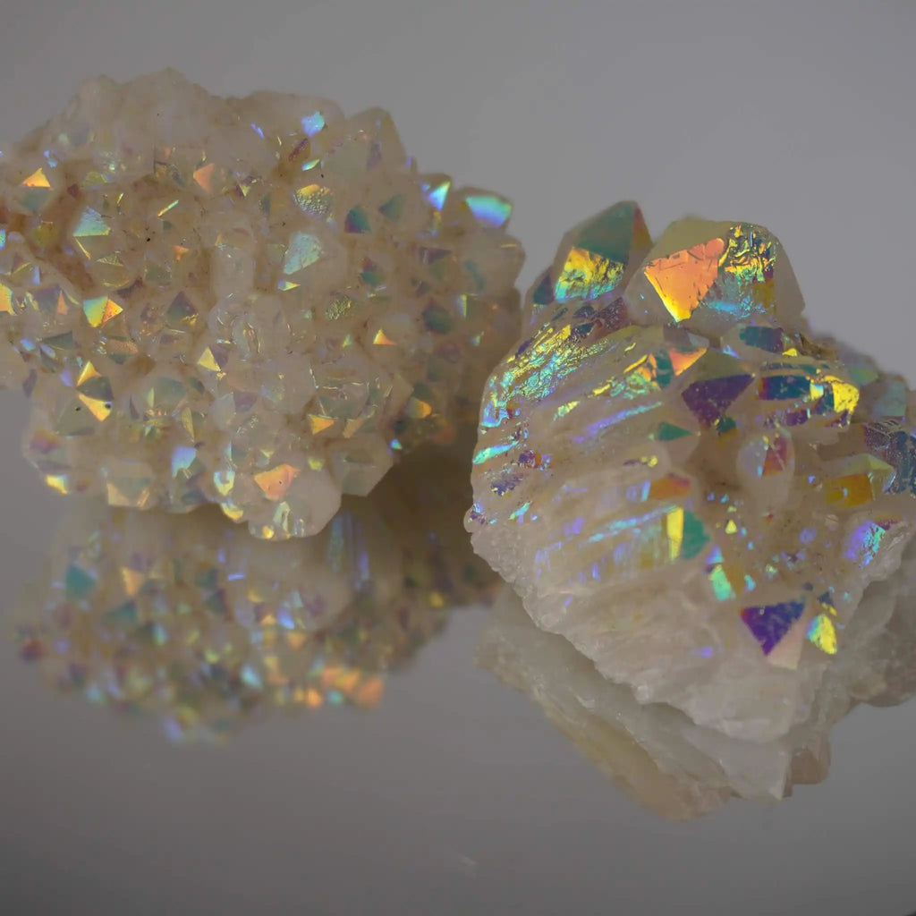 Zwei Angel Aura Cluster Kristalle mit intensivem Regenbogenschimmer auf spiegelnder Fläche