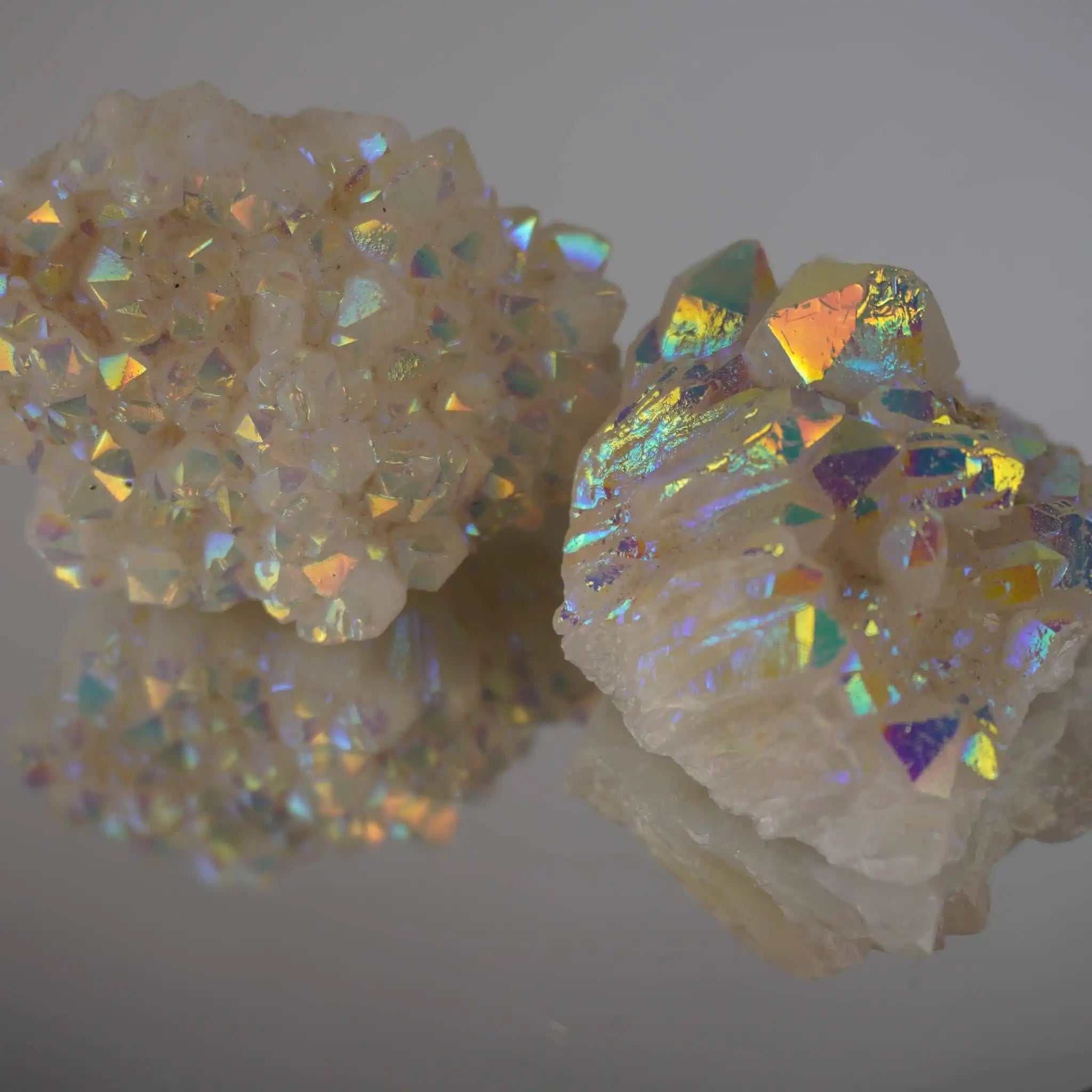 Zwei Angel Aura Cluster Kristalle mit intensivem Regenbogenschimmer auf spiegelnder Fläche