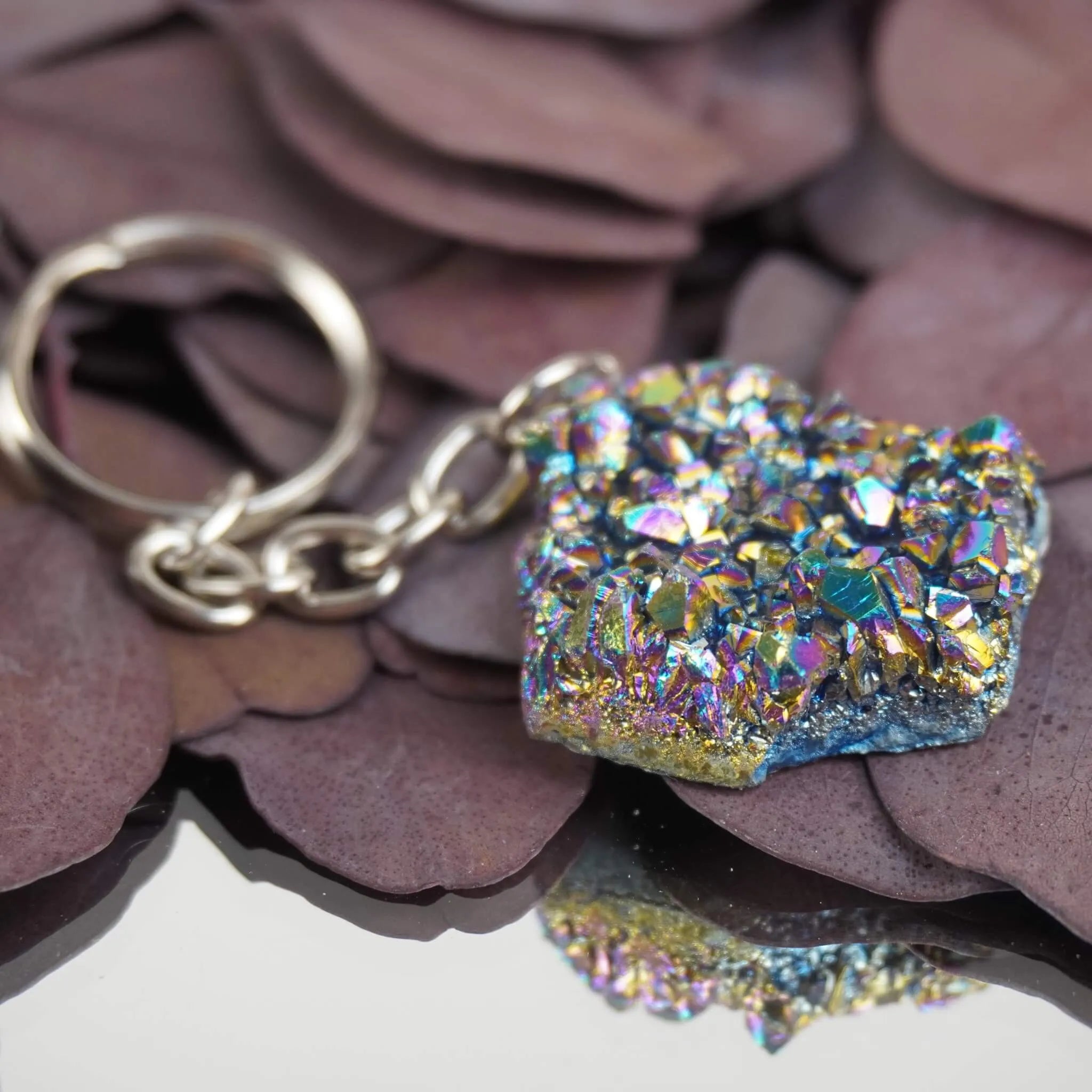 Regenbogenfarbener Aqua Aura Druse Schlüsselanhänger mit Spiegelung auf dunklen Blättern