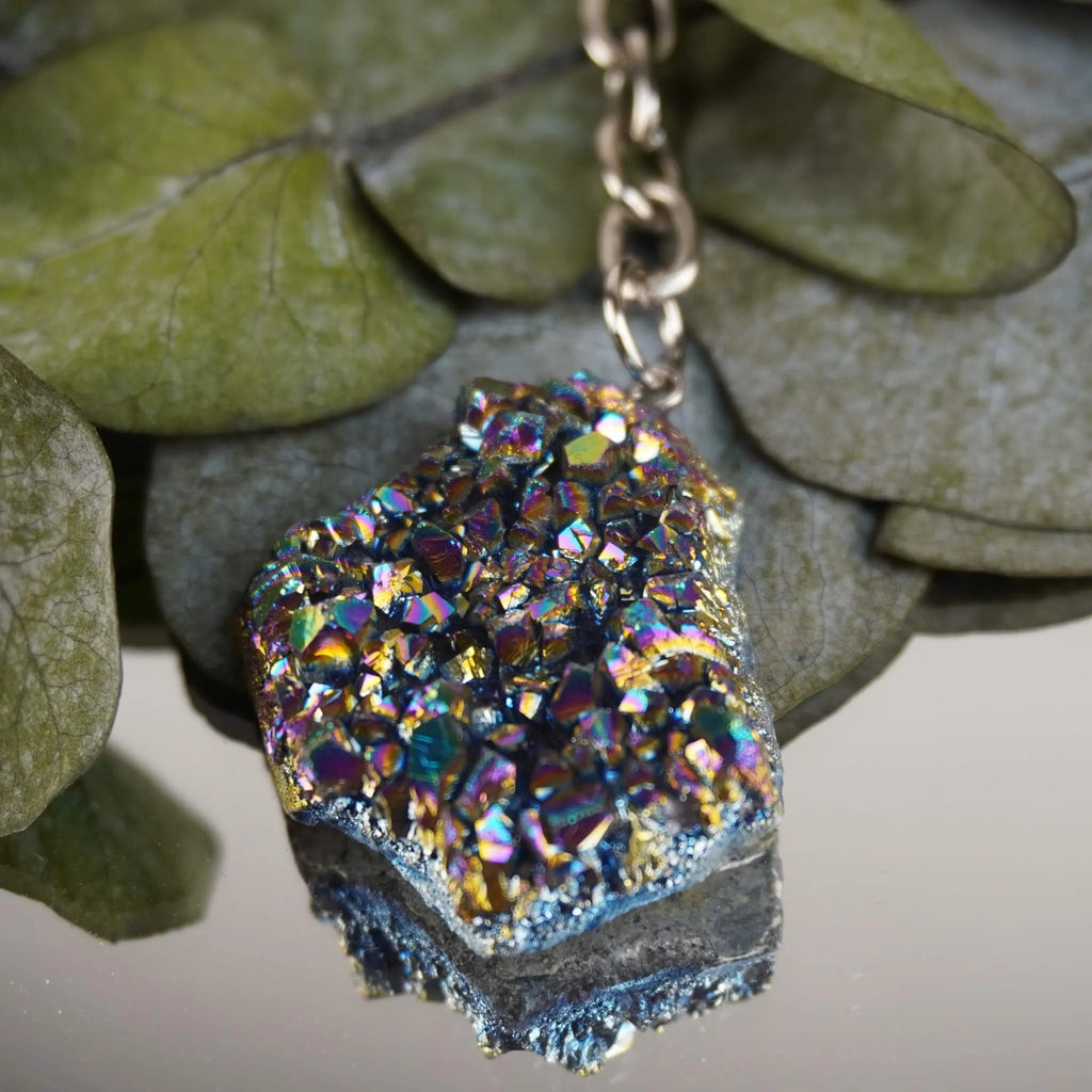 Aqua Aura Druse Schlüsselanhänger mit intensiv schillernder Oberfläche vor grünen Eukalyptusblättern dekoriert