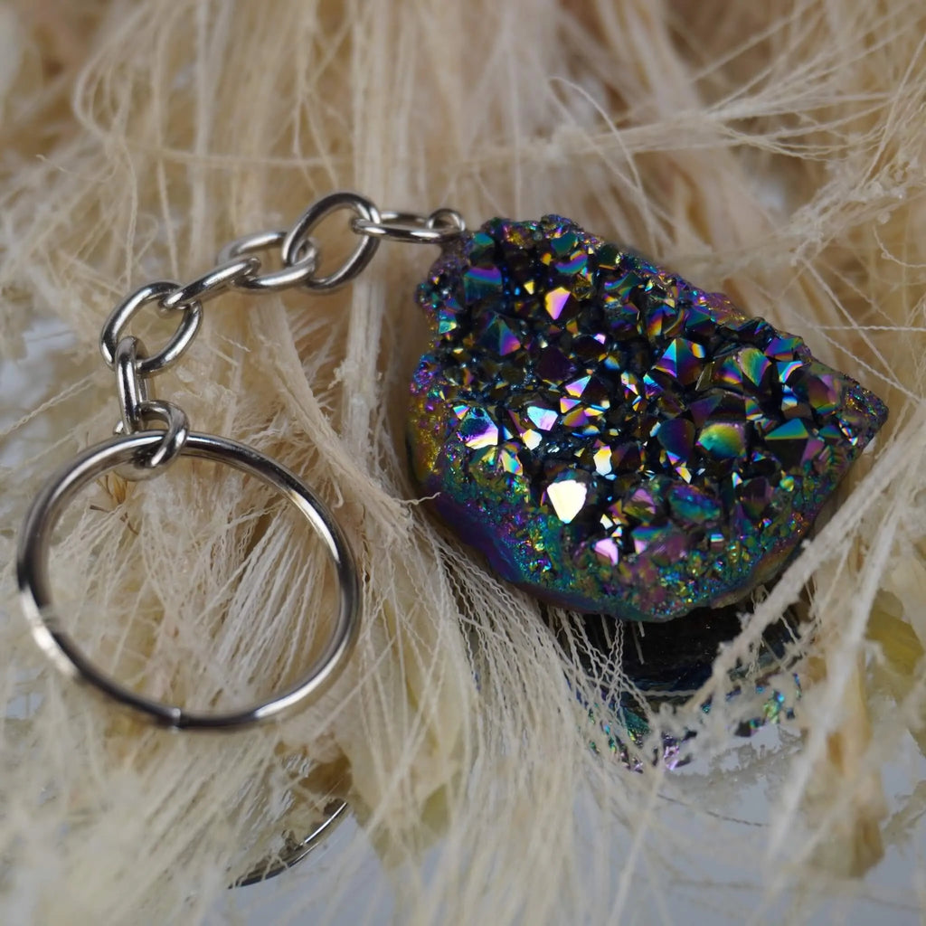 Aqua Aura Druse Schlüsselanhänger mit bunt schimmernden Kristallen auf hellen Naturfasern