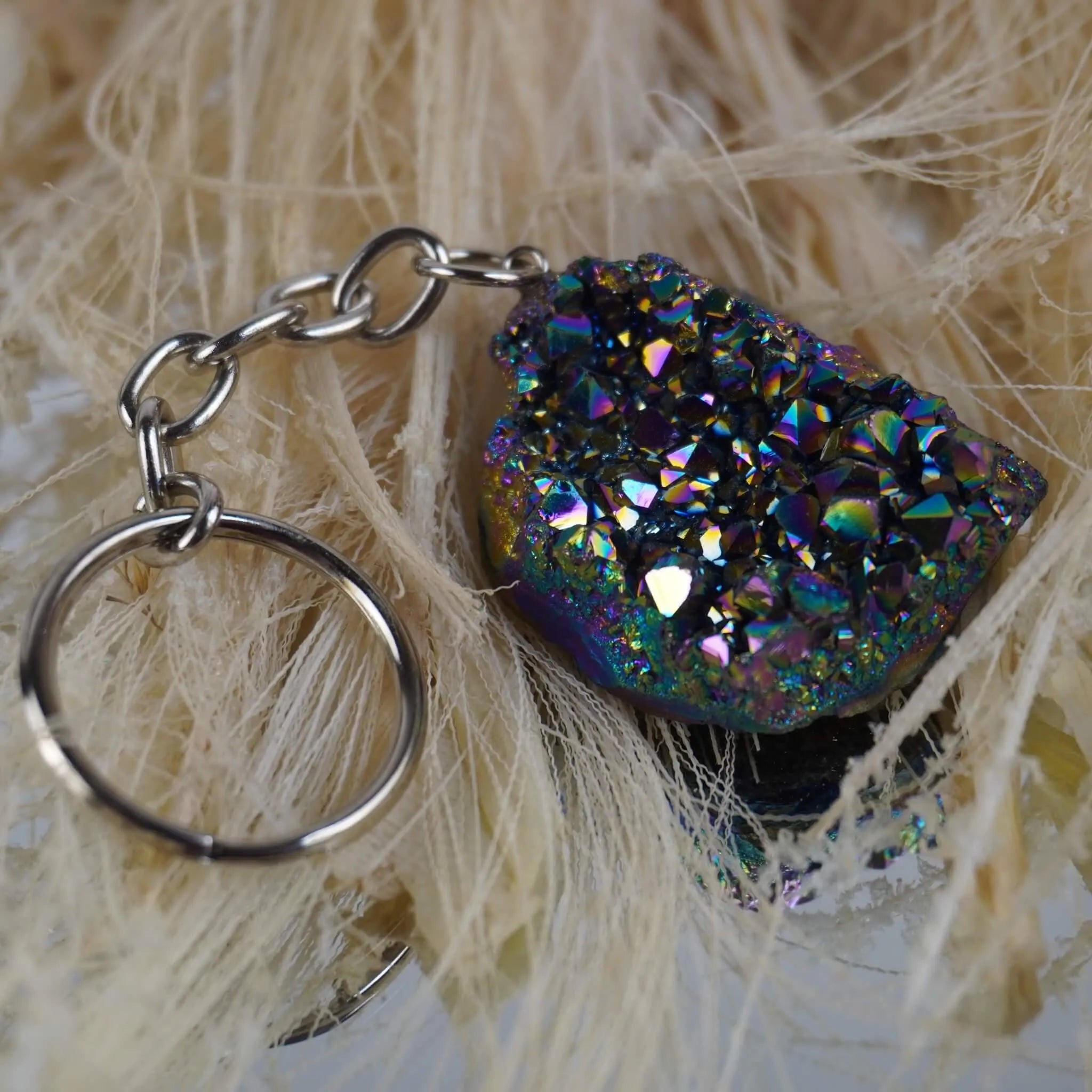 Aqua Aura Druse Schlüsselanhänger mit bunt schimmernden Kristallen auf hellen Naturfasern