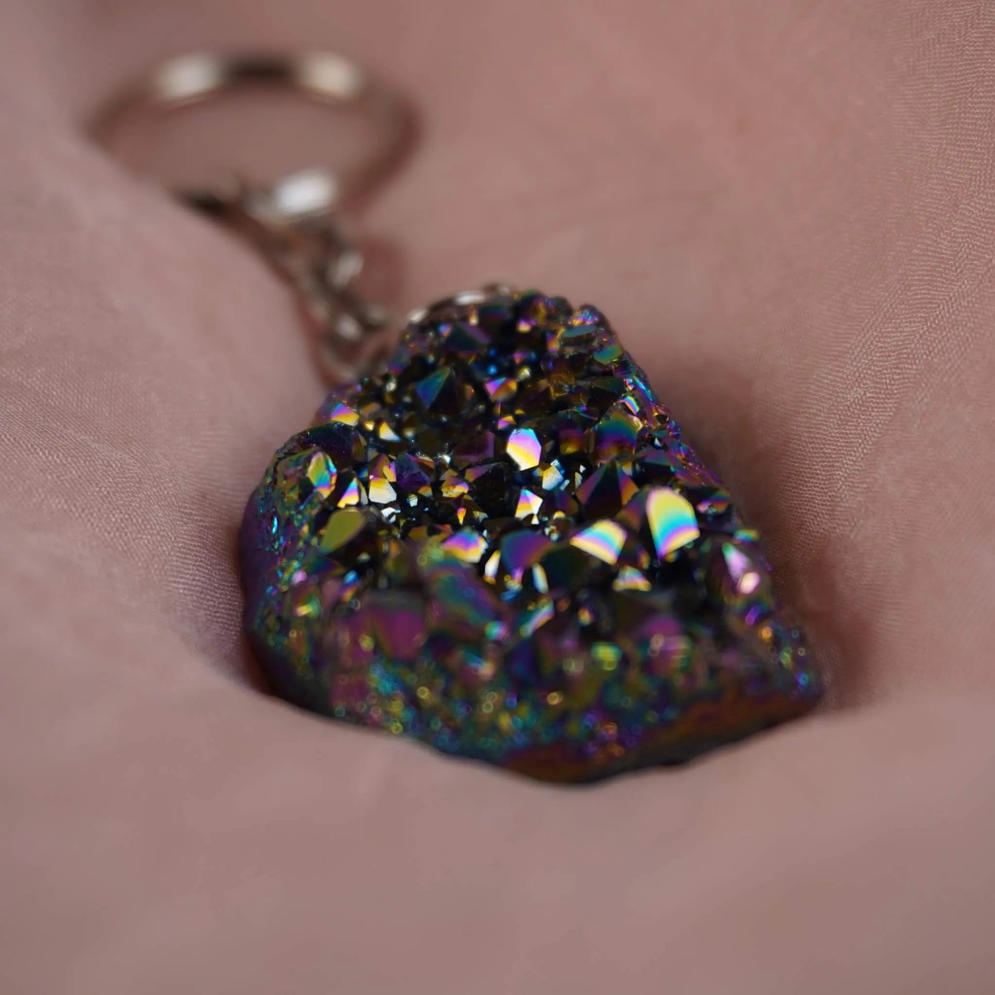 Bunt schimmernder Aqua Aura Druse Schlüsselanhänger präsentiert auf rosafarbenem Stoff