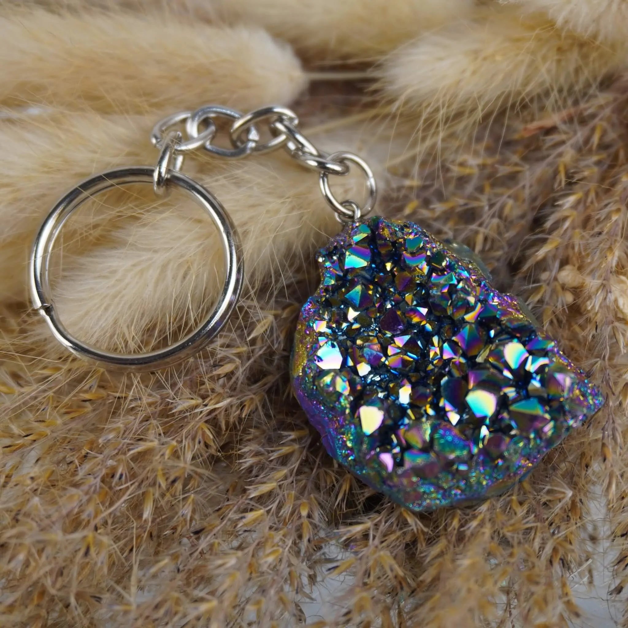 Regenbogenfarbener Aqua Aura Druse Schlüsselanhänger mit Metallkette auf beigen Trockenpflanzen