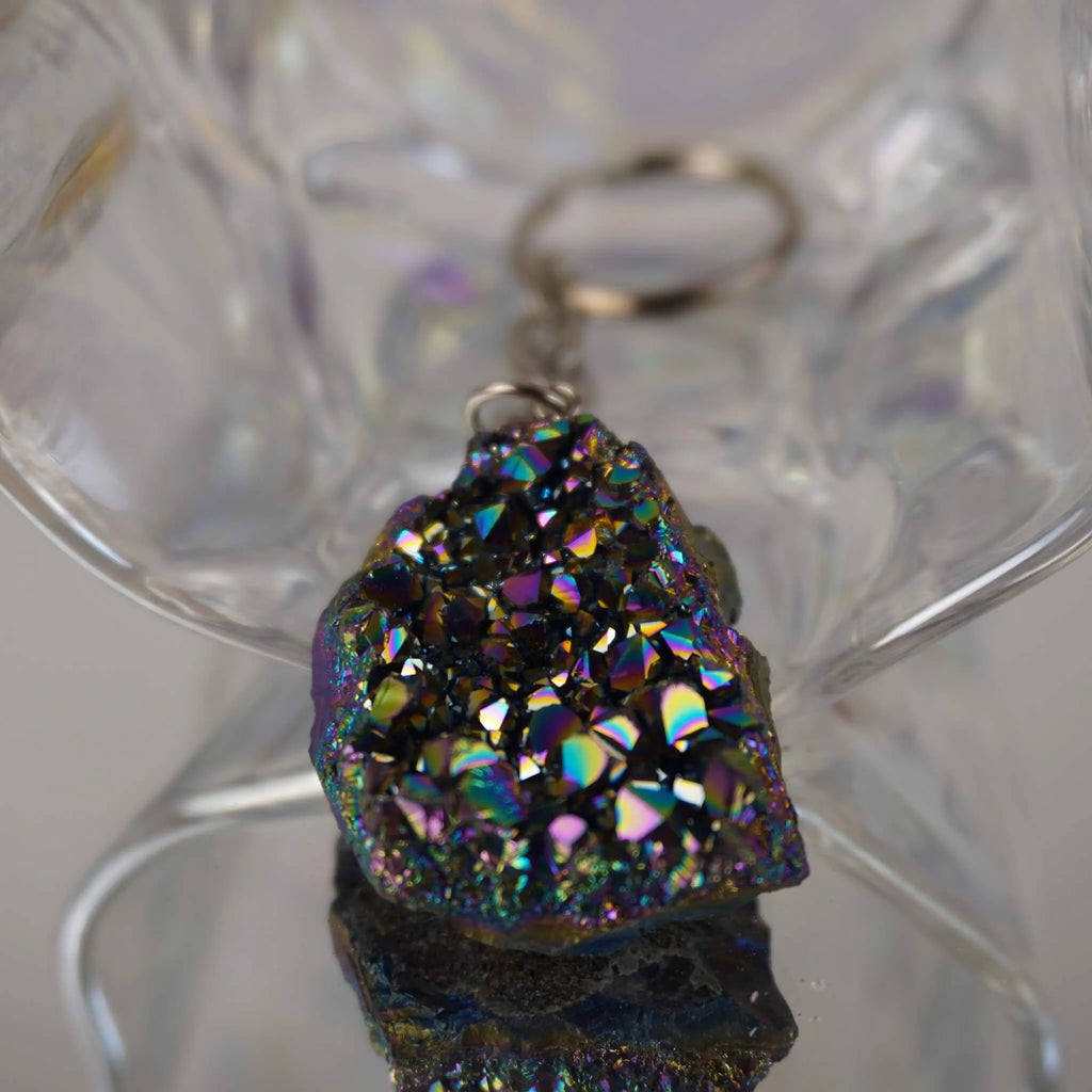 Aqua Aura Druse Schlüsselanhänger mit intensivem  Regenbogenschimmer vor transparenter Glasdeko