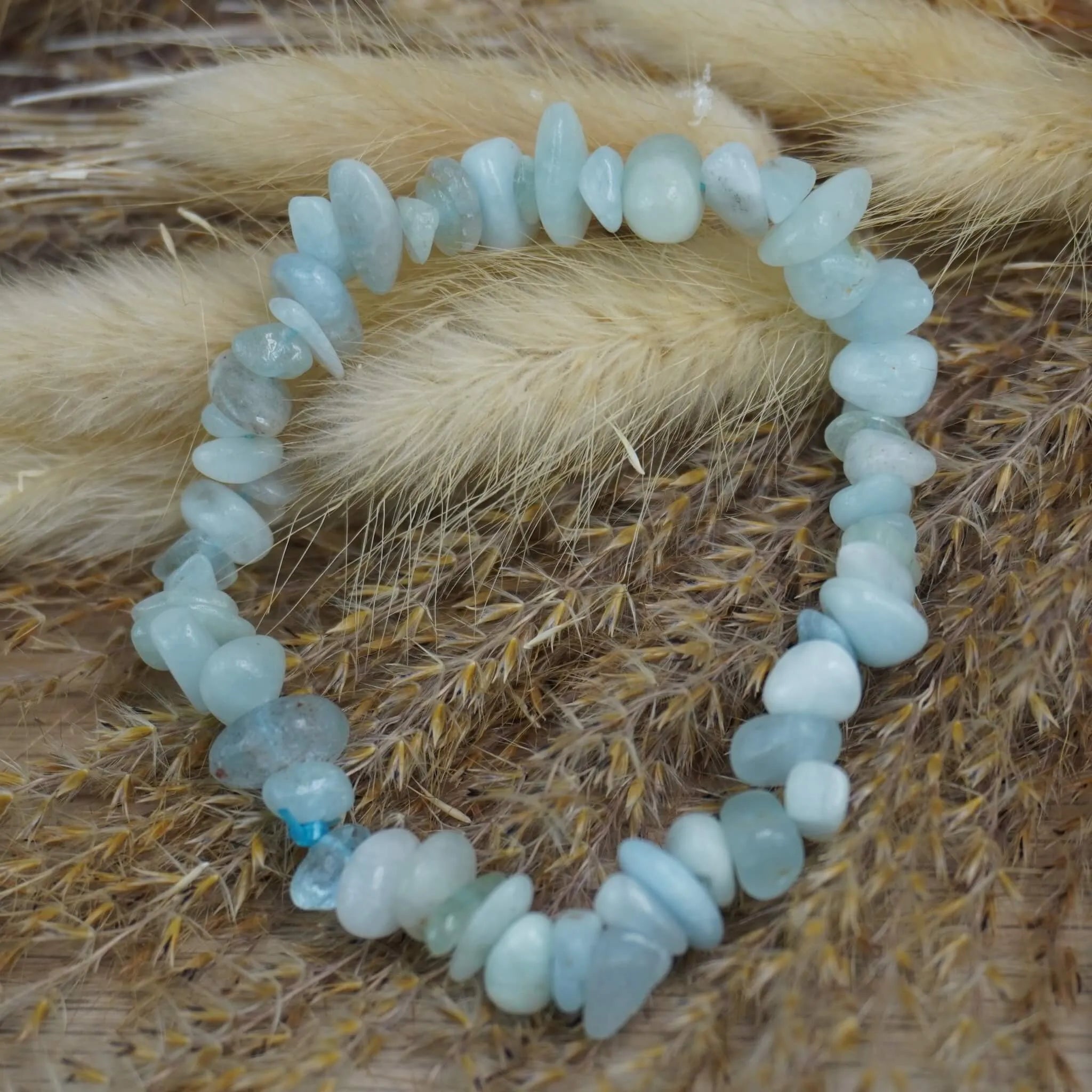 Aquamarin‑Splitterarmband dekoriert auf beigen Trockenblumen und Gräsern