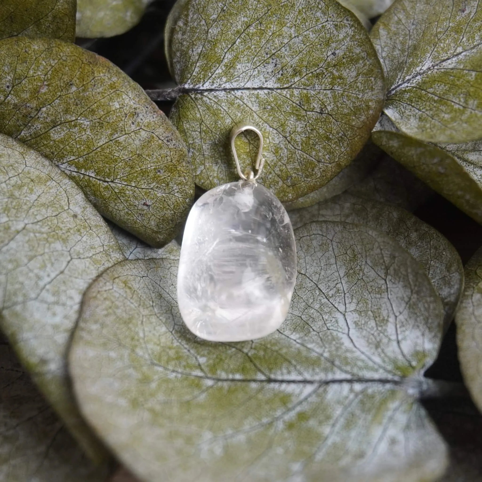 Klarer Bergkristall Trommelstein Kettenanhänger mit Silber Öse auf grünen Eukalyptusblättern