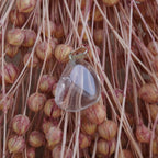 Klarer Bergkristall Trommelstein Kettenanhänger dekoriert vor rosa Trockenblumen