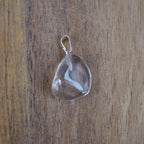 Klarer Bergkristall Trommelstein Kettenanhänger mit silberner Öse vor Holzuntergrund