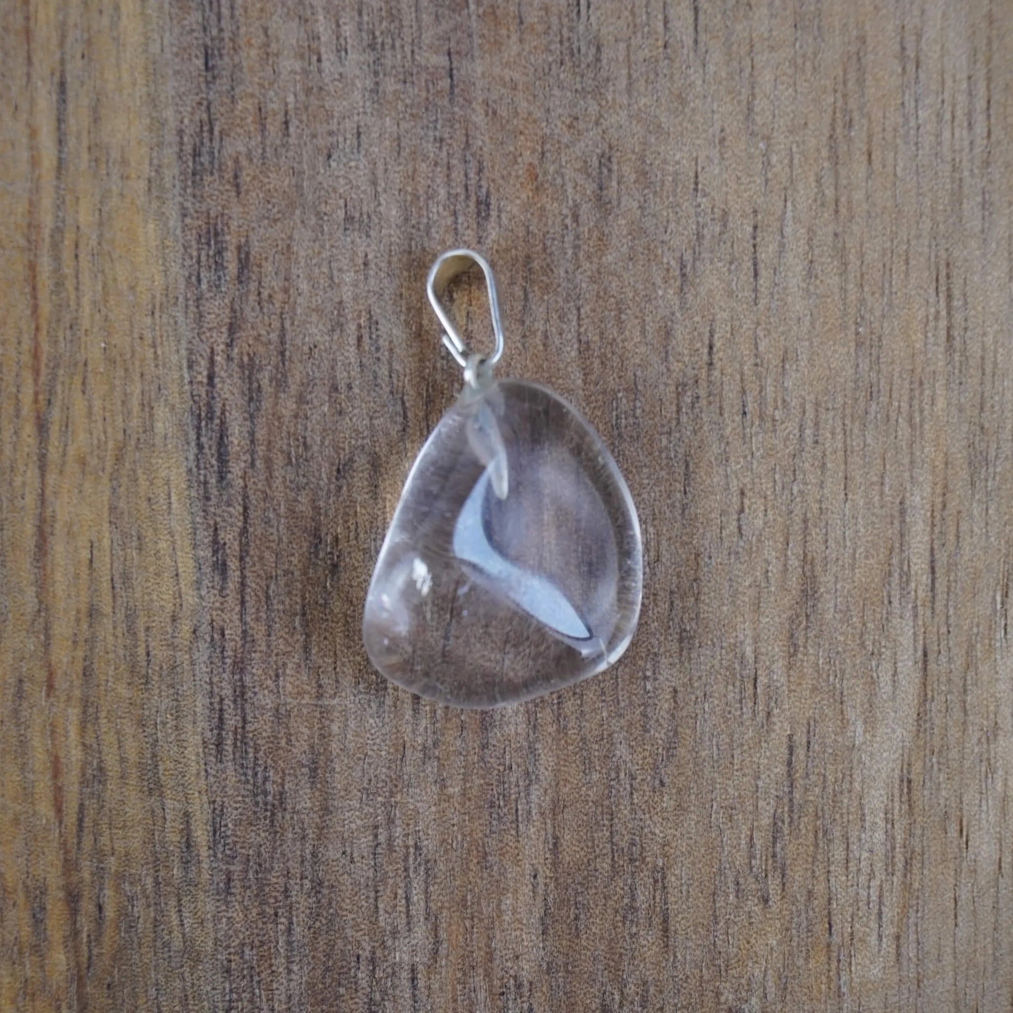 Klarer Bergkristall Trommelstein Kettenanhänger mit silberner Öse vor Holzuntergrund