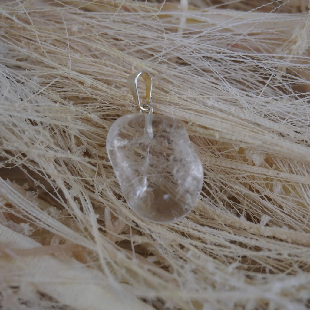 Klarer Bergkristall Trommelstein Kettenanhänger mit silberner Öse auf hellen Naturfasern arrangiert