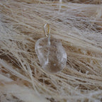 Klarer Bergkristall Trommelstein Kettenanhänger mit silberner Öse auf hellen Naturfasern arrangiert