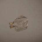 Klarer Bergkristall Trommelstein Kettenanhänger mit Silber-Öse auf spiegelnder Fläche