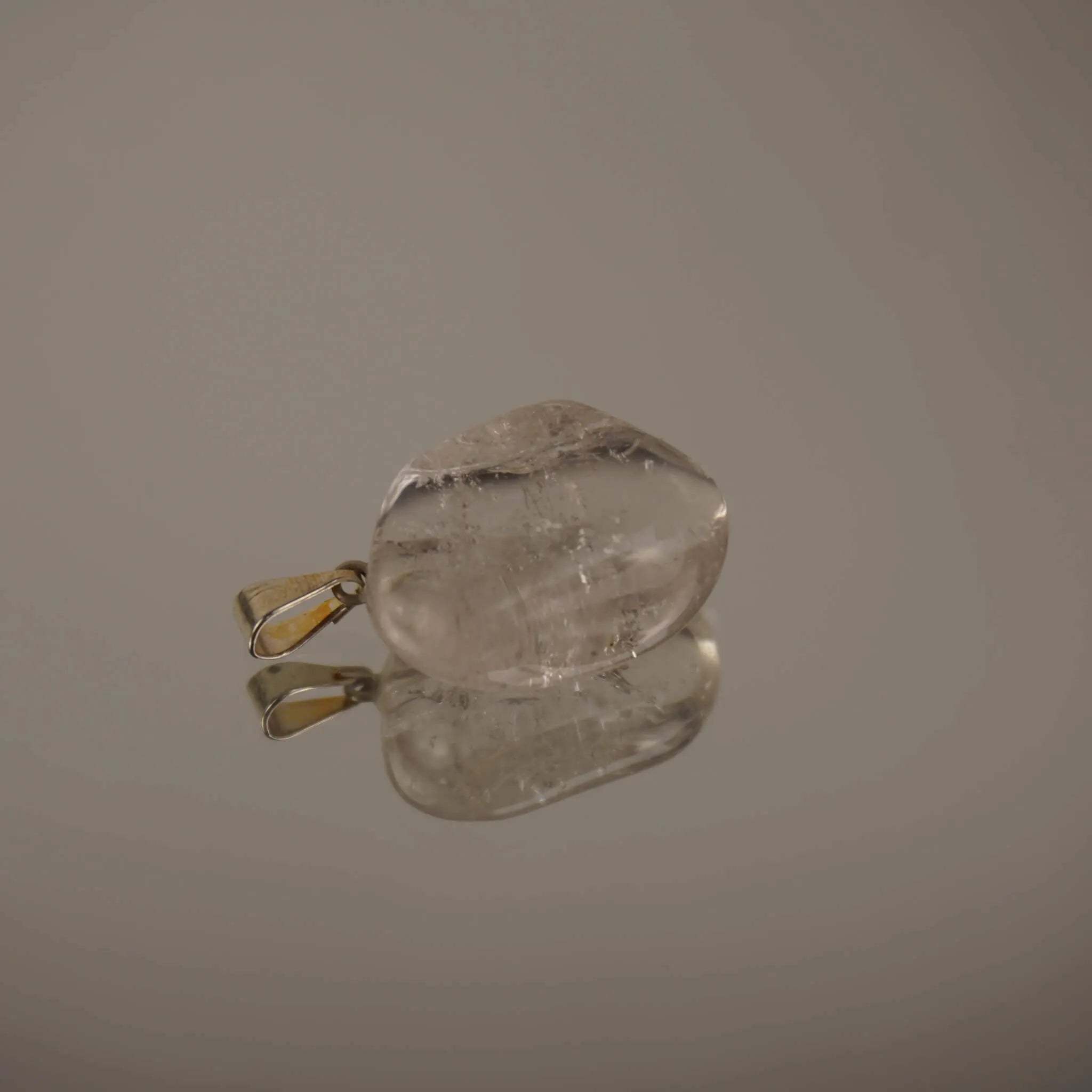 Klarer Bergkristall Trommelstein Kettenanhänger mit Silber-Öse auf spiegelnder Fläche