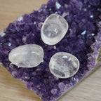 Drei Bergkristall Trommelsteine auf einer Amethystdruse platziert