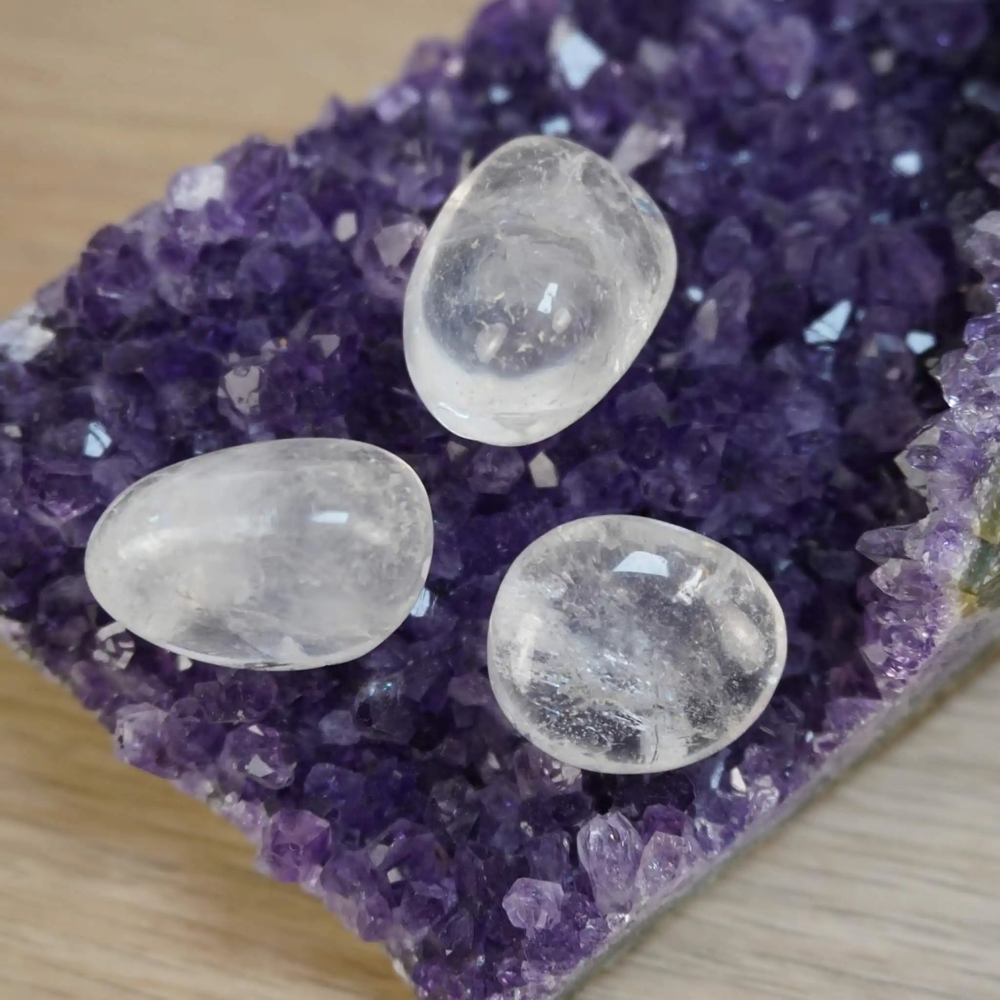 Drei Bergkristall Trommelsteine auf einer Amethystdruse platziert