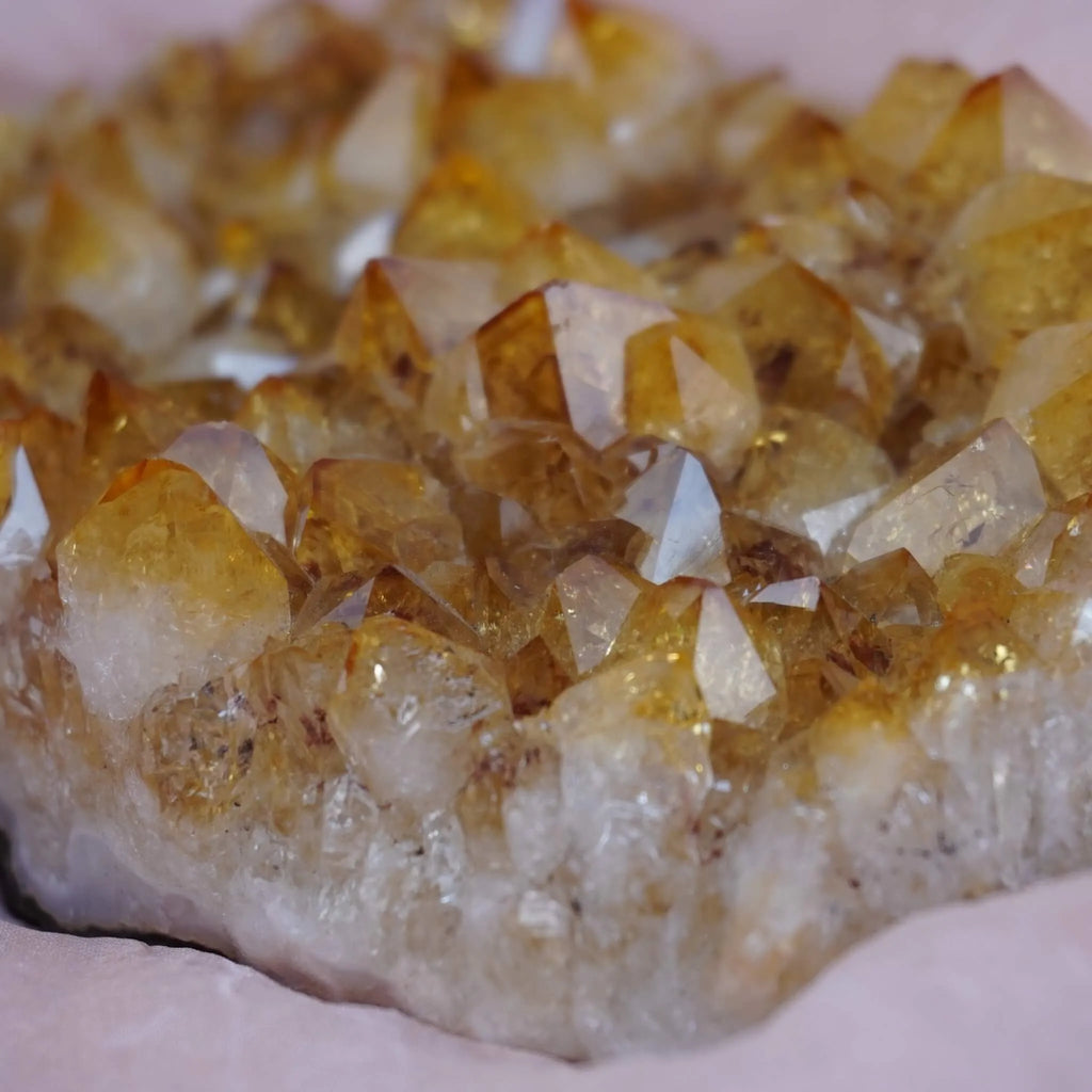 Nahaufnahme eines Citrin Clusters mit warmen Gelbtönen auf rosafarbenem Stoff