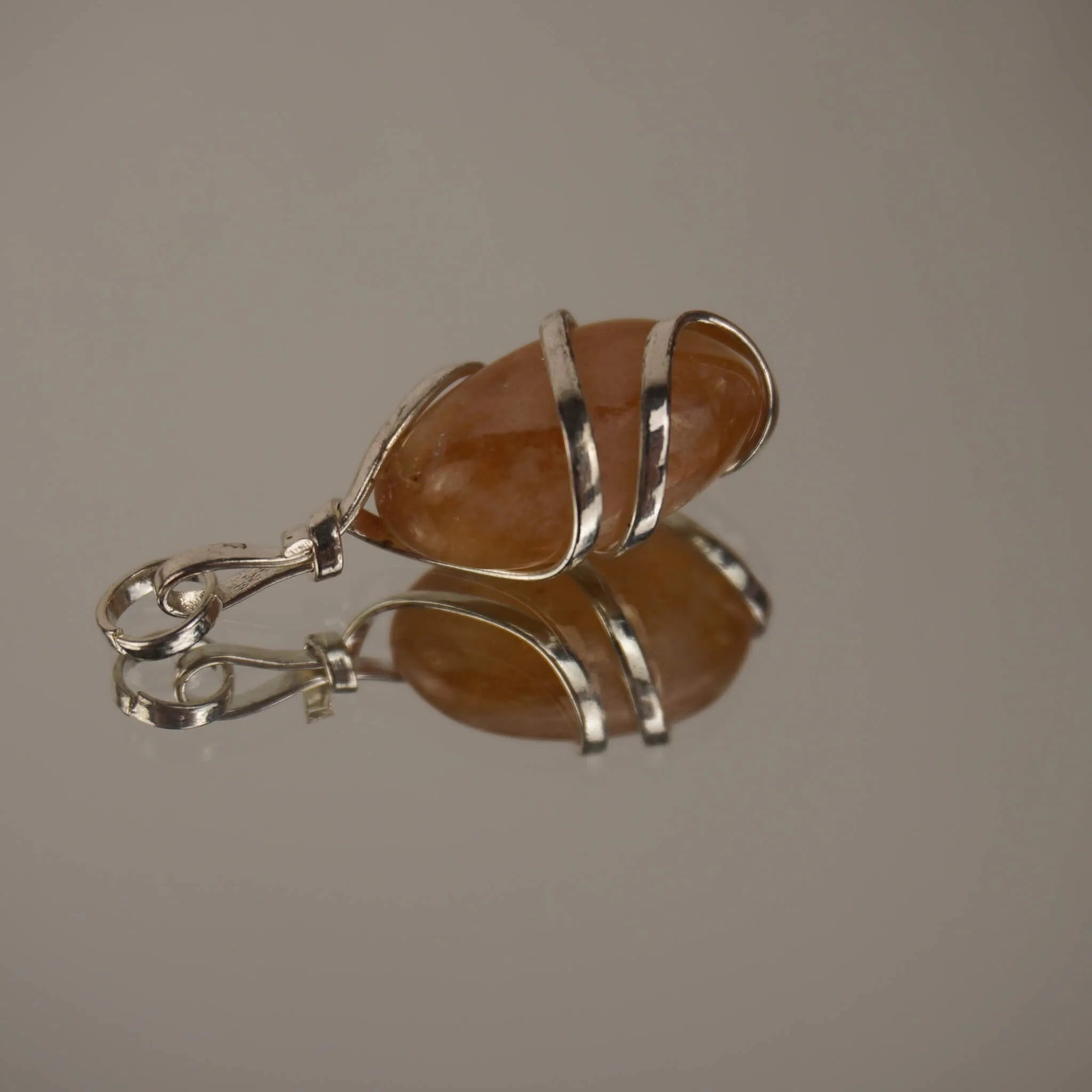 Liegender Citrin Kettenanhänger mit silberfarbener Spiralfassung und Spiegelung auf glänzender Fläche