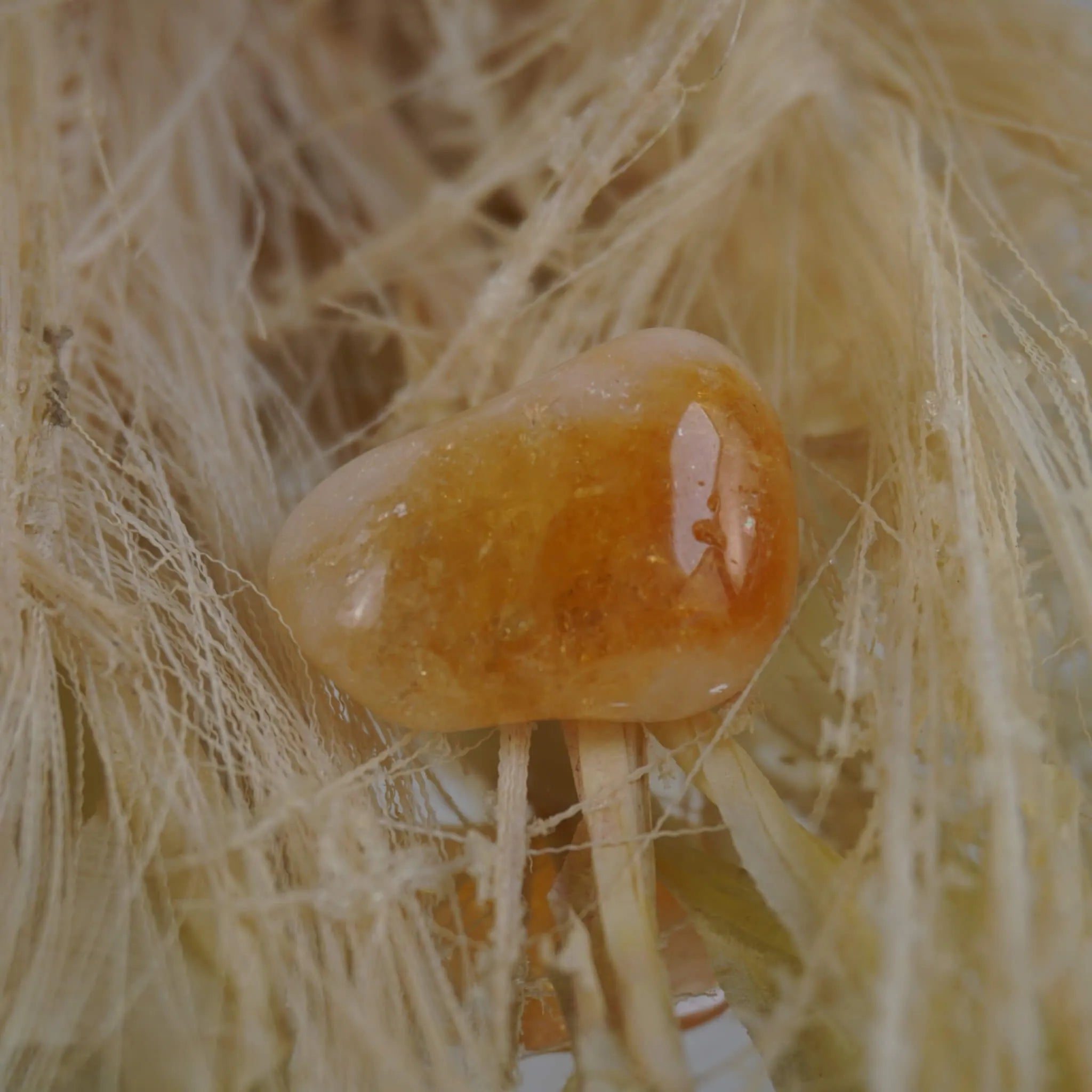 Intensiv orangegelber Citrin Trommelstein auf hellen Naturfasern