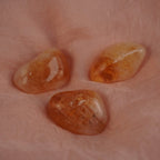 Drei glänzende Citrin Trommelsteine auf weich gefaltetem rosafarbenem Stoff