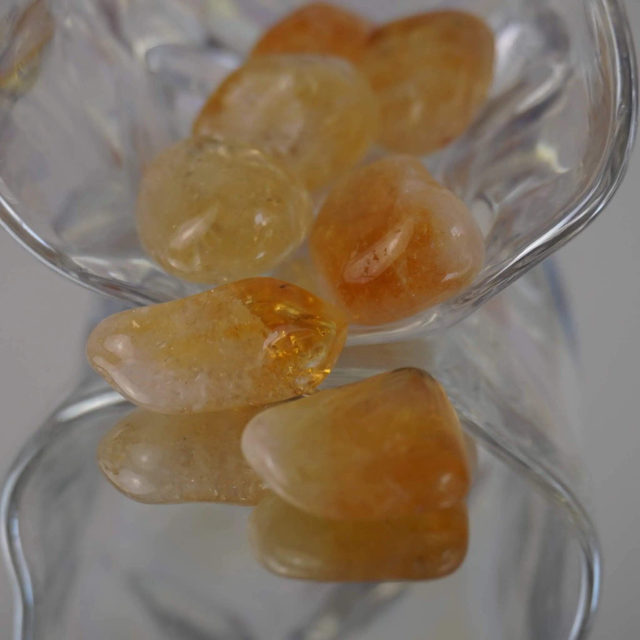 Mehrere gelb orangene Citrin Trommelsteine in einer dekorativen Glasform mit Spiegelung