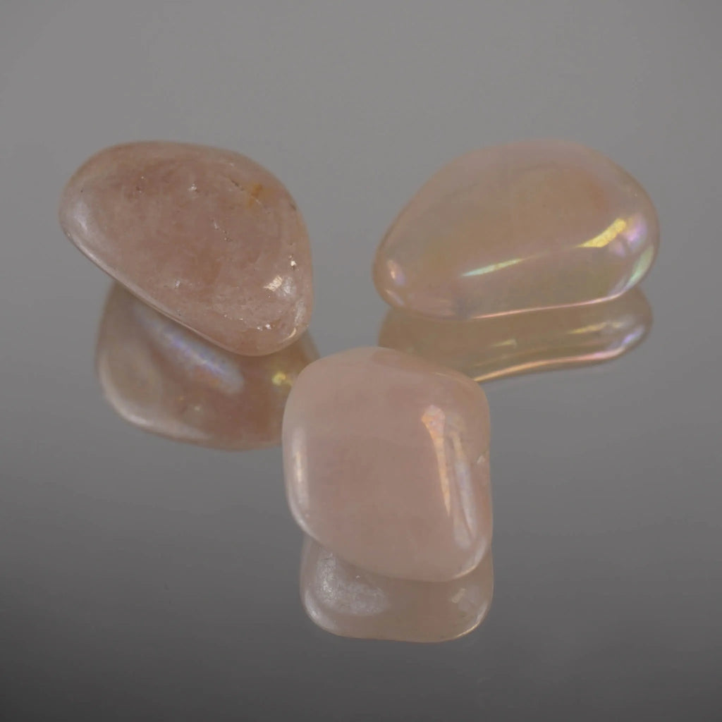 Drei rosa Angel Aura Trommelsteine mit Regenbogenglanz und Spiegelung auf Glasfläche