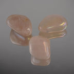 Drei rosa Angel Aura Trommelsteine mit Regenbogenglanz und Spiegelung auf Glasfläche