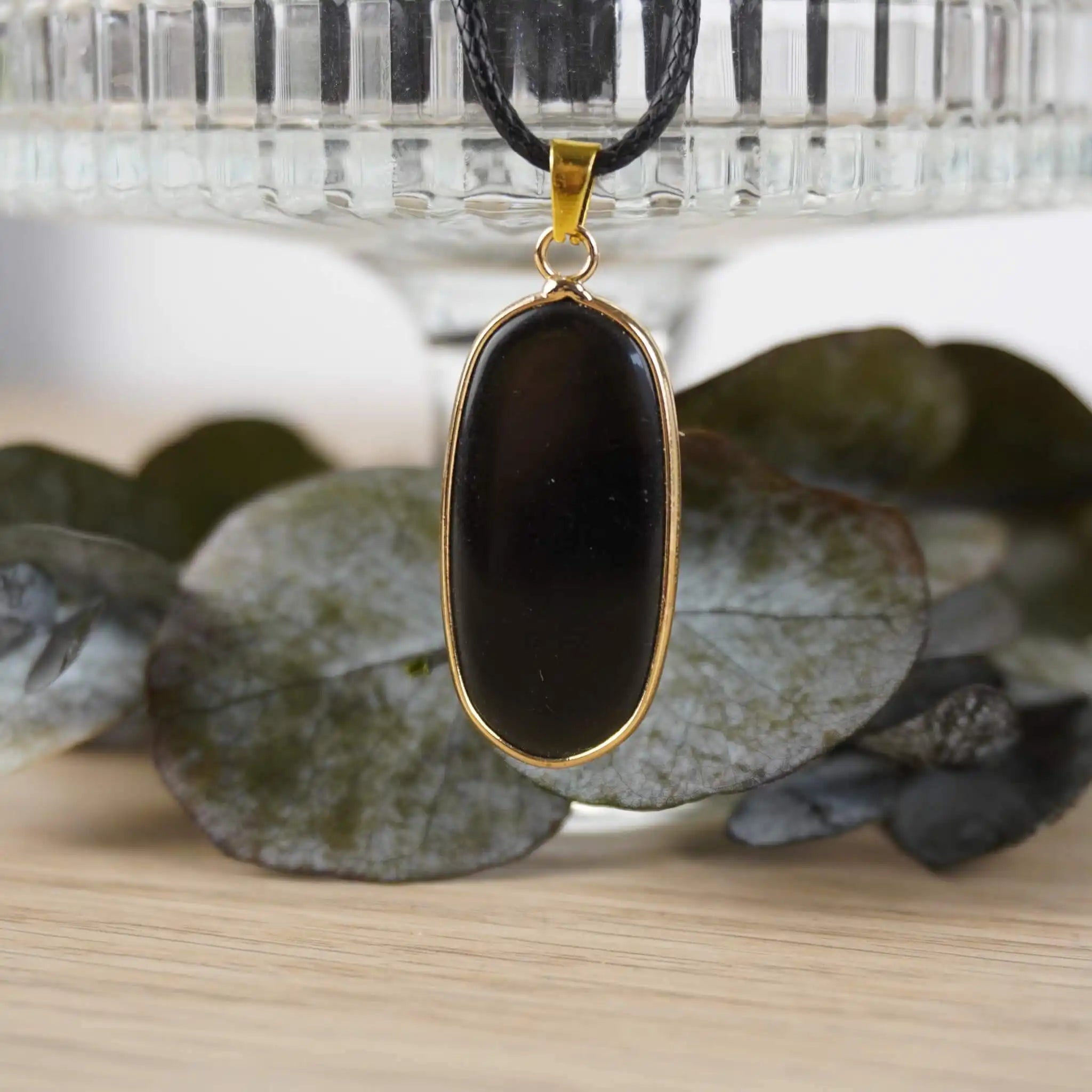 Halskette mit schwarzem Onyx-Anhänger, elegant präsentiert vor Glasgefäß und Blättern