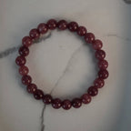 Erdbeerquarz Kugelarmband auf weißem Marmorhintergrund