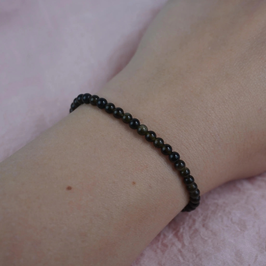 Goldener Obsidian Kugelarmband dezent am Handgelenk vor rosa Hintergrund