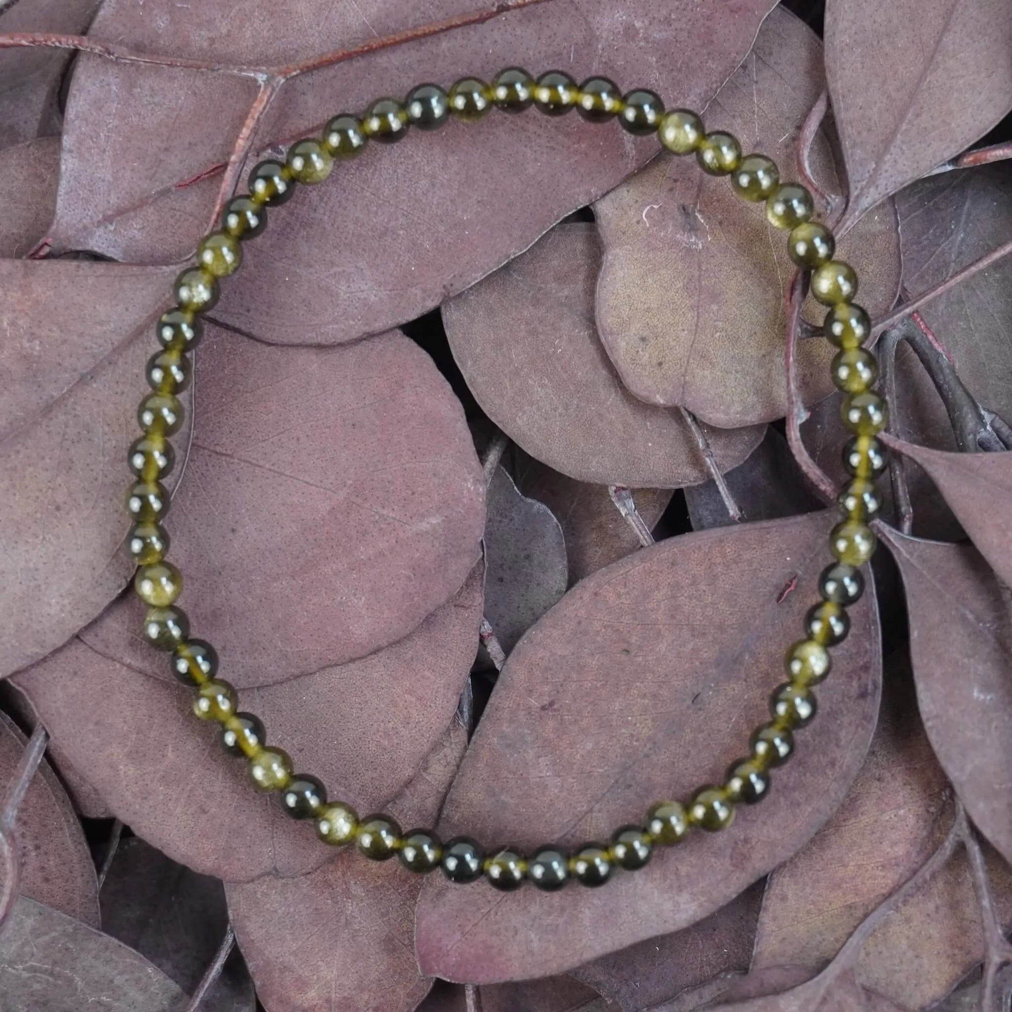 Goldener Obsidian Kugelarmband auf violett-braunen Blättern modern arrangiert