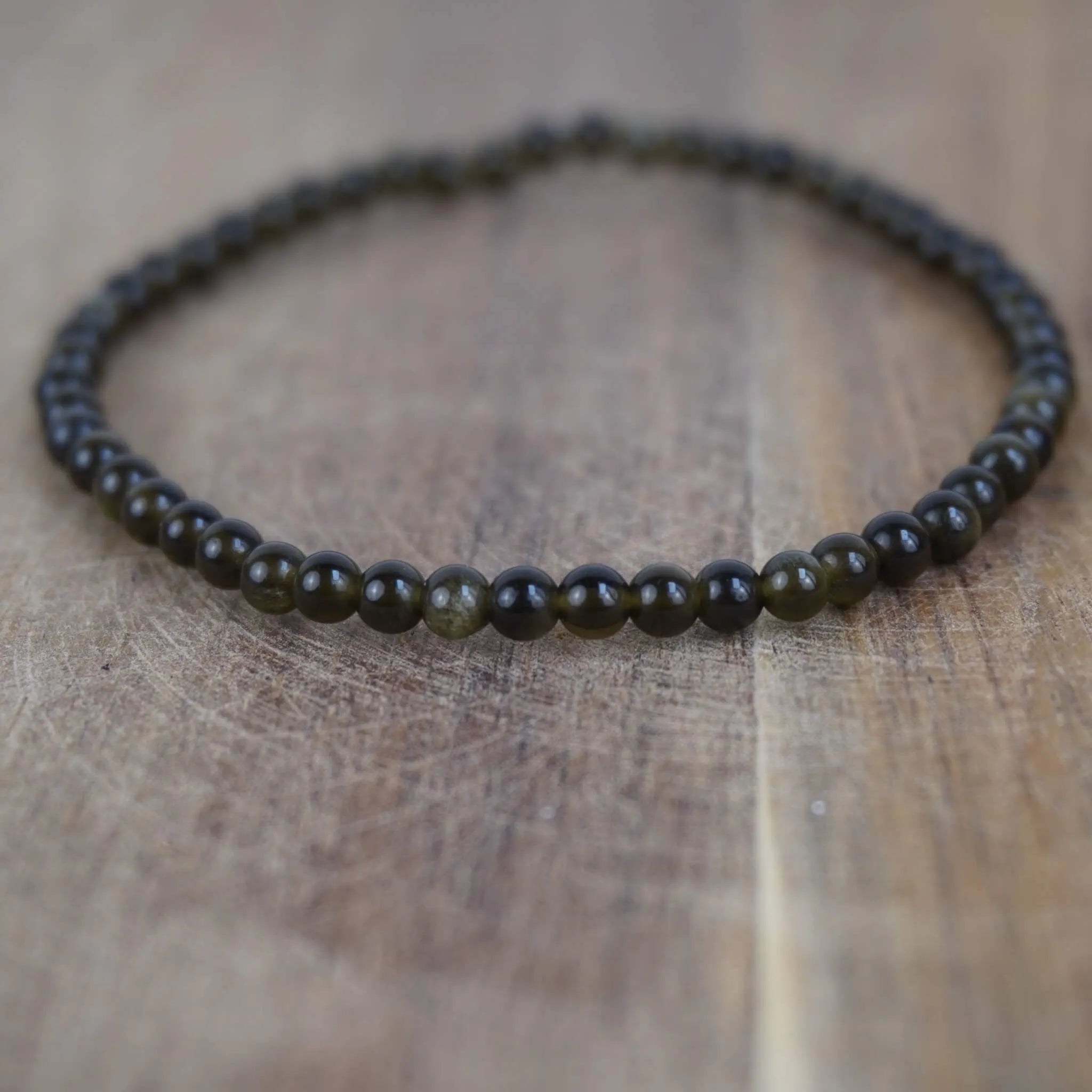 Goldener Obsidian Kugelarmband auf warmer Holzoberfläche im Nahaufnahme-Detail