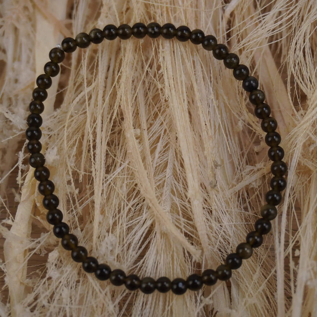 Goldener Obsidian Kugelarmband auf hellem Naturfaserdekor mit sichtbarer Struktur