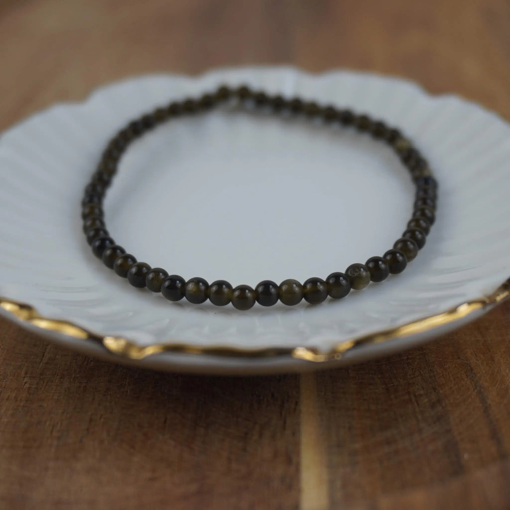 Goldener Obsidian Kugelarmband auf weißem Schmuckteller mit feinem Goldrand