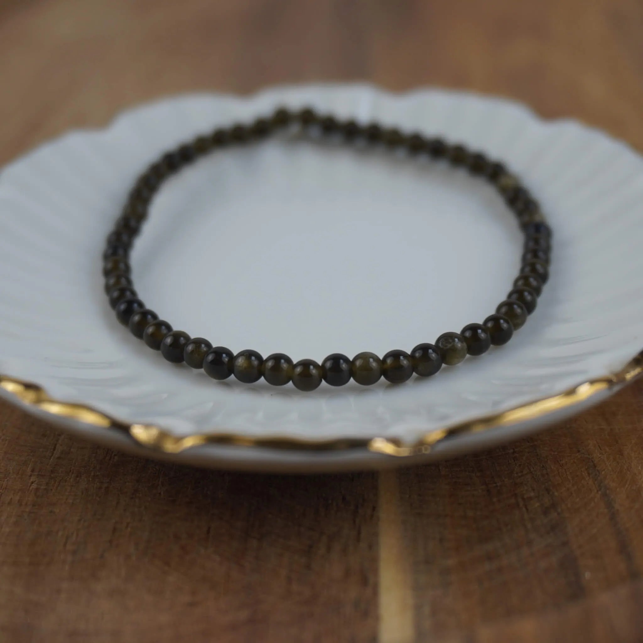 Goldener Obsidian Kugelarmband auf weißem Schmuckteller mit feinem Goldrand