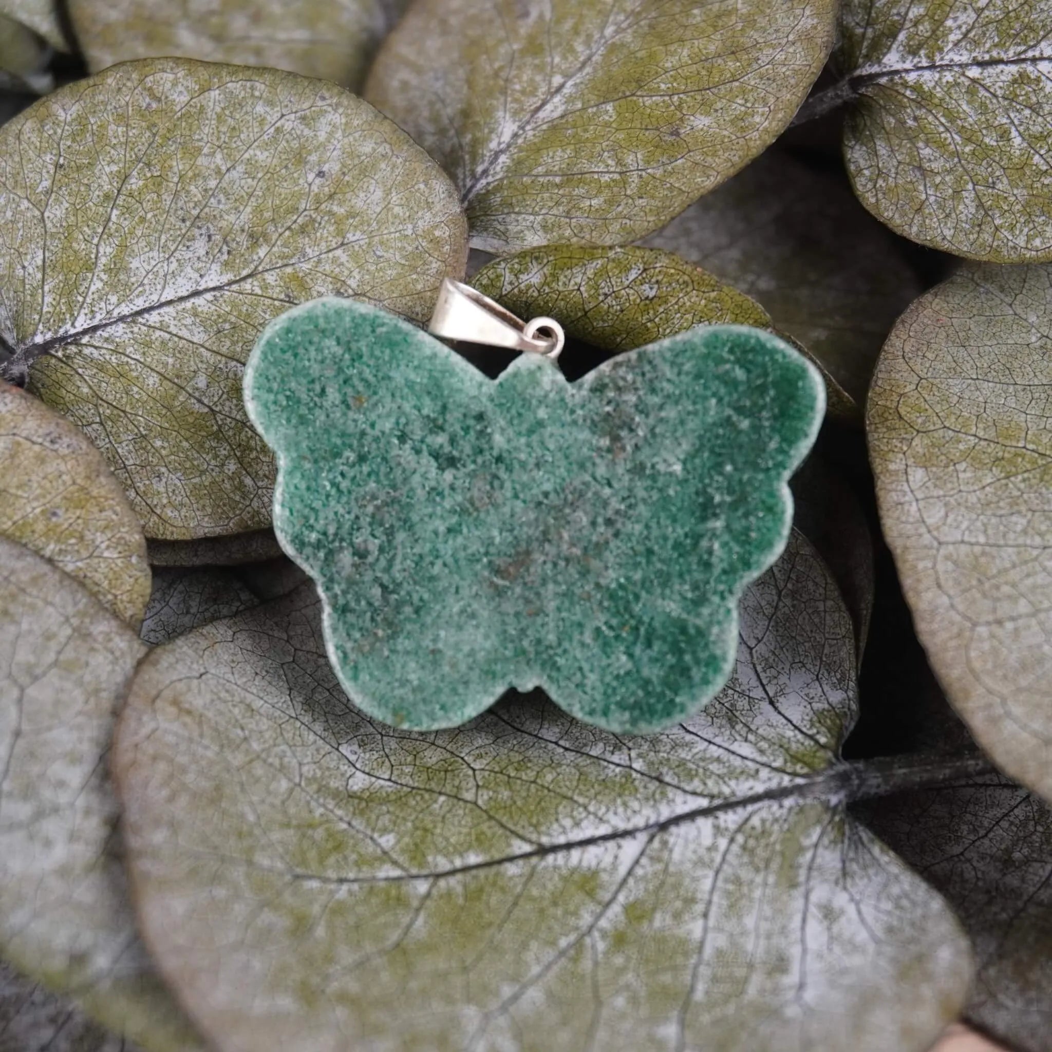 Grüner Aventurin Schmetterling Kettenanhänger auf grünen Eukalyptusblättern arrangiert